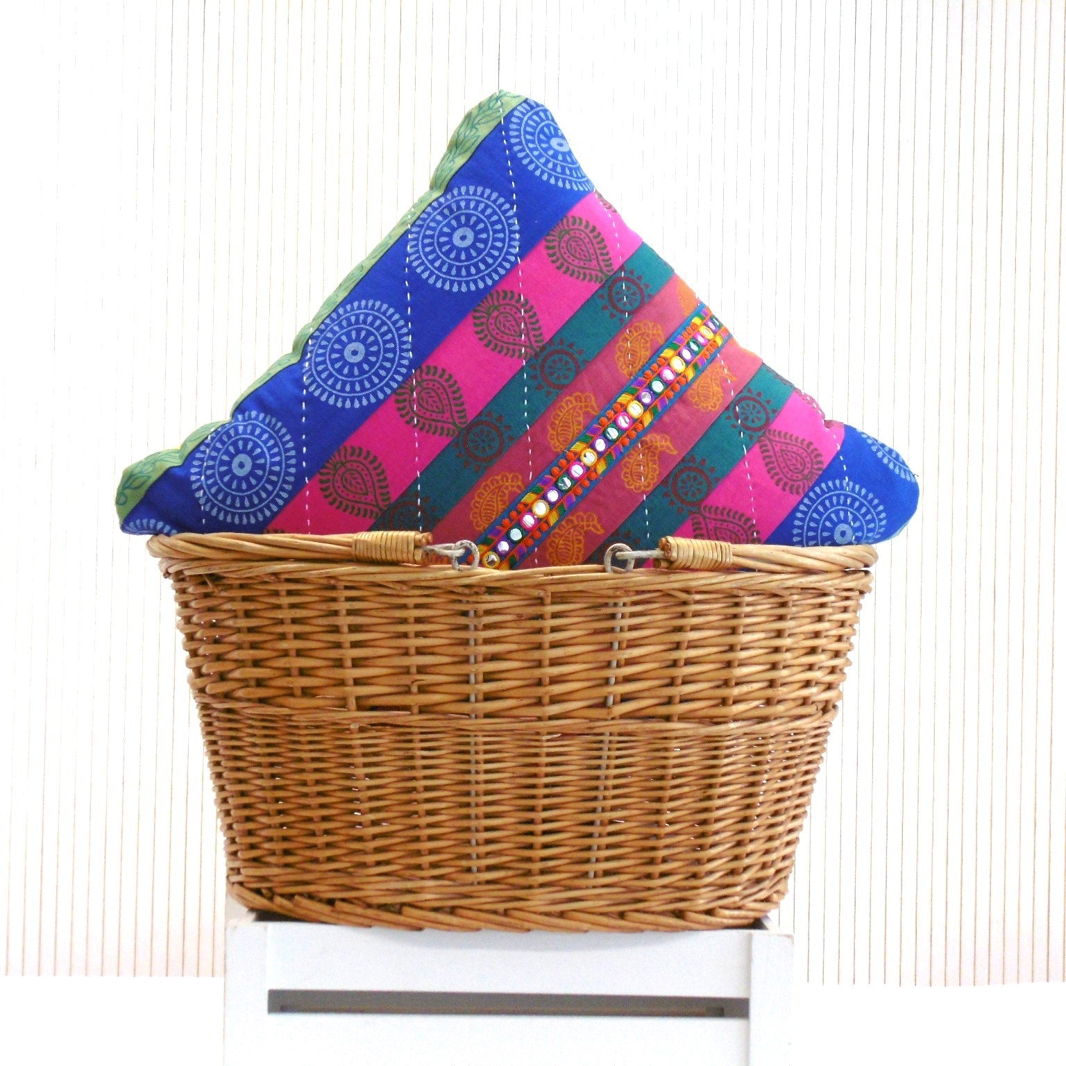 Two hand block printed Mela Magic patchwork cushions in blue pink and teal with mirror trim, colour coordinated front and back, in a wicker basket by Naila Ahmad London