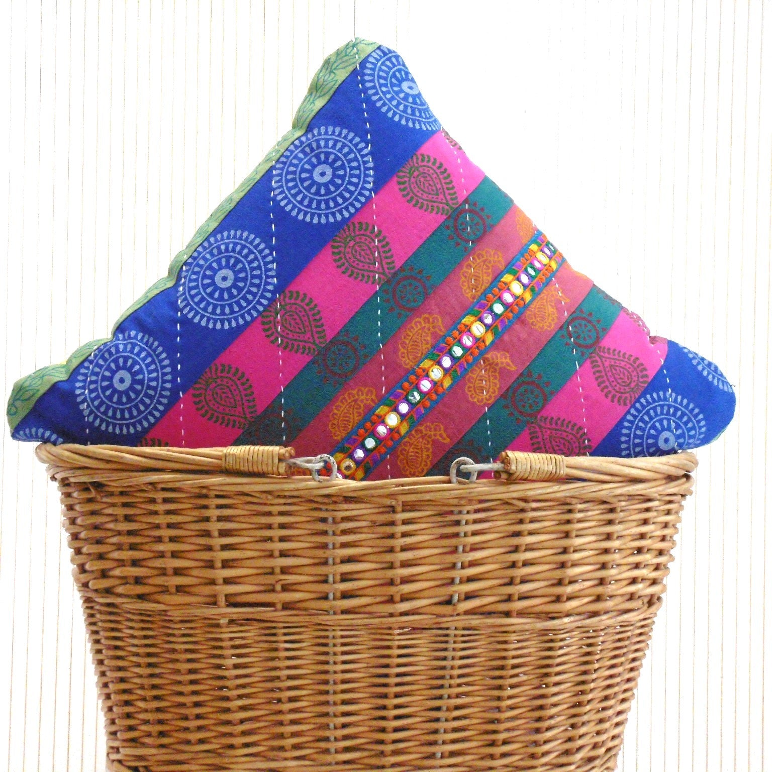 Two Mela Magic patchwork cushions in vibrant blue pink and teal with mirror trim, showing colour coordinated reverse, in a wicker basket by Naila Ahmad London