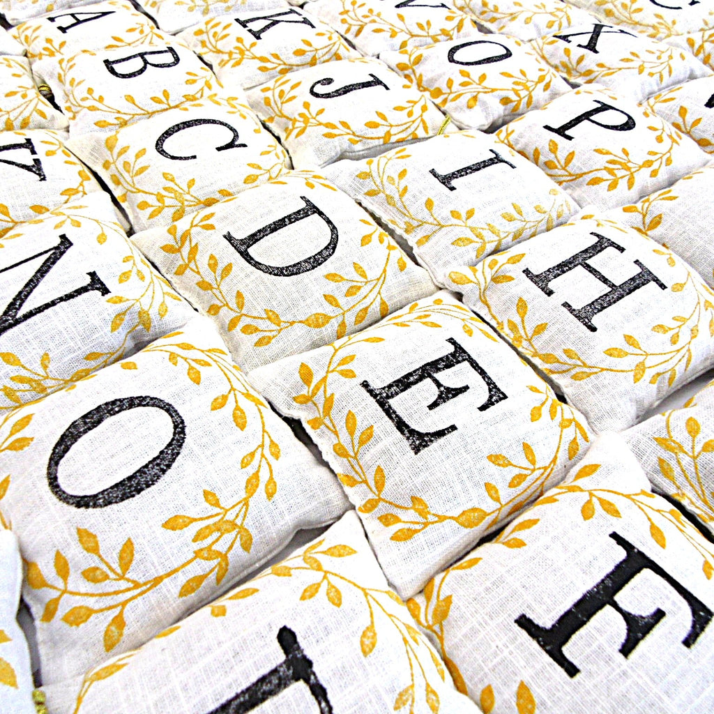 Flat lay of hand block printed alphabet lavender sachets showing all letters with golden leaf design, by Naila Ahmad London