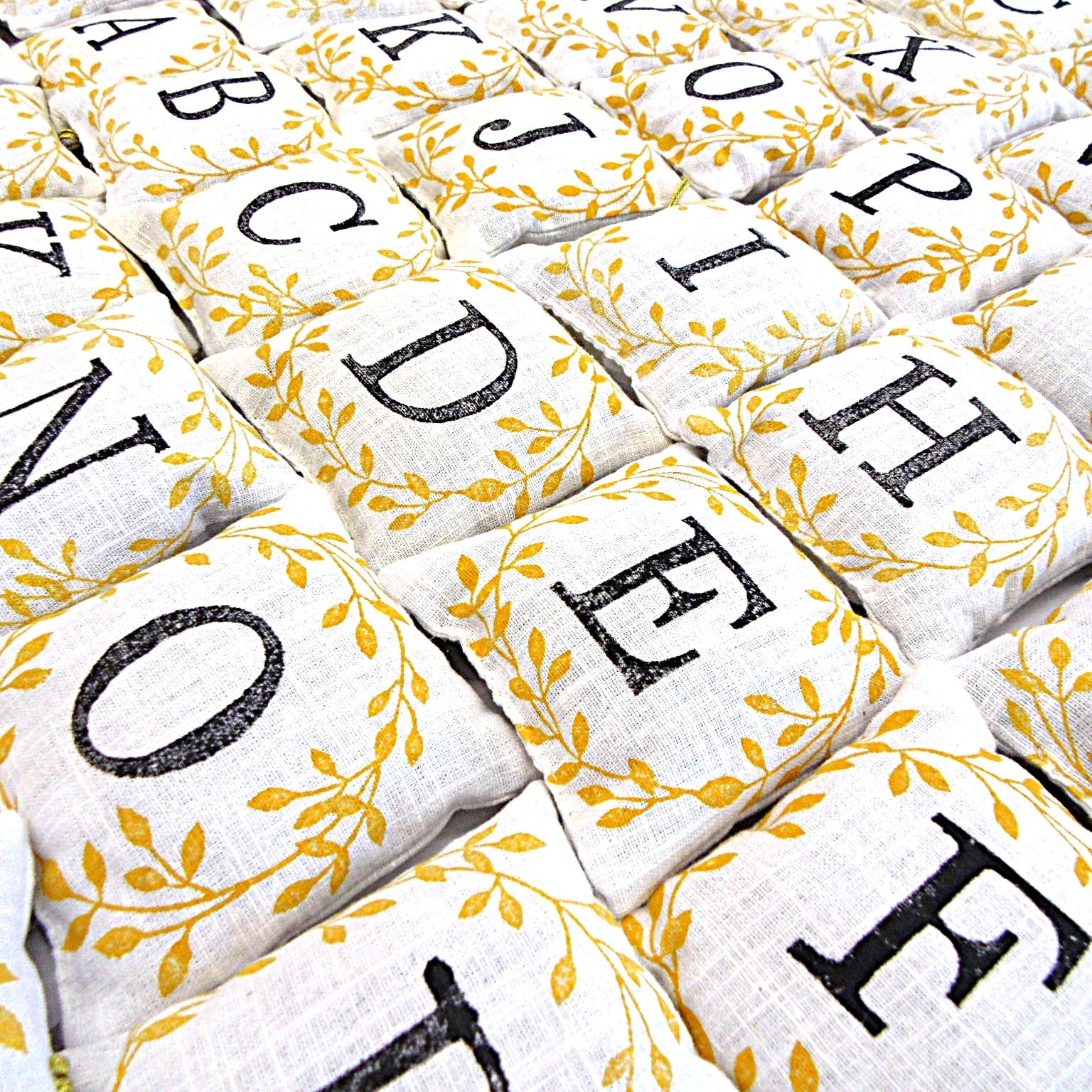 Flat lay of hand block printed alphabet lavender sachets showing all letters with golden leaf design, by Naila Ahmad London