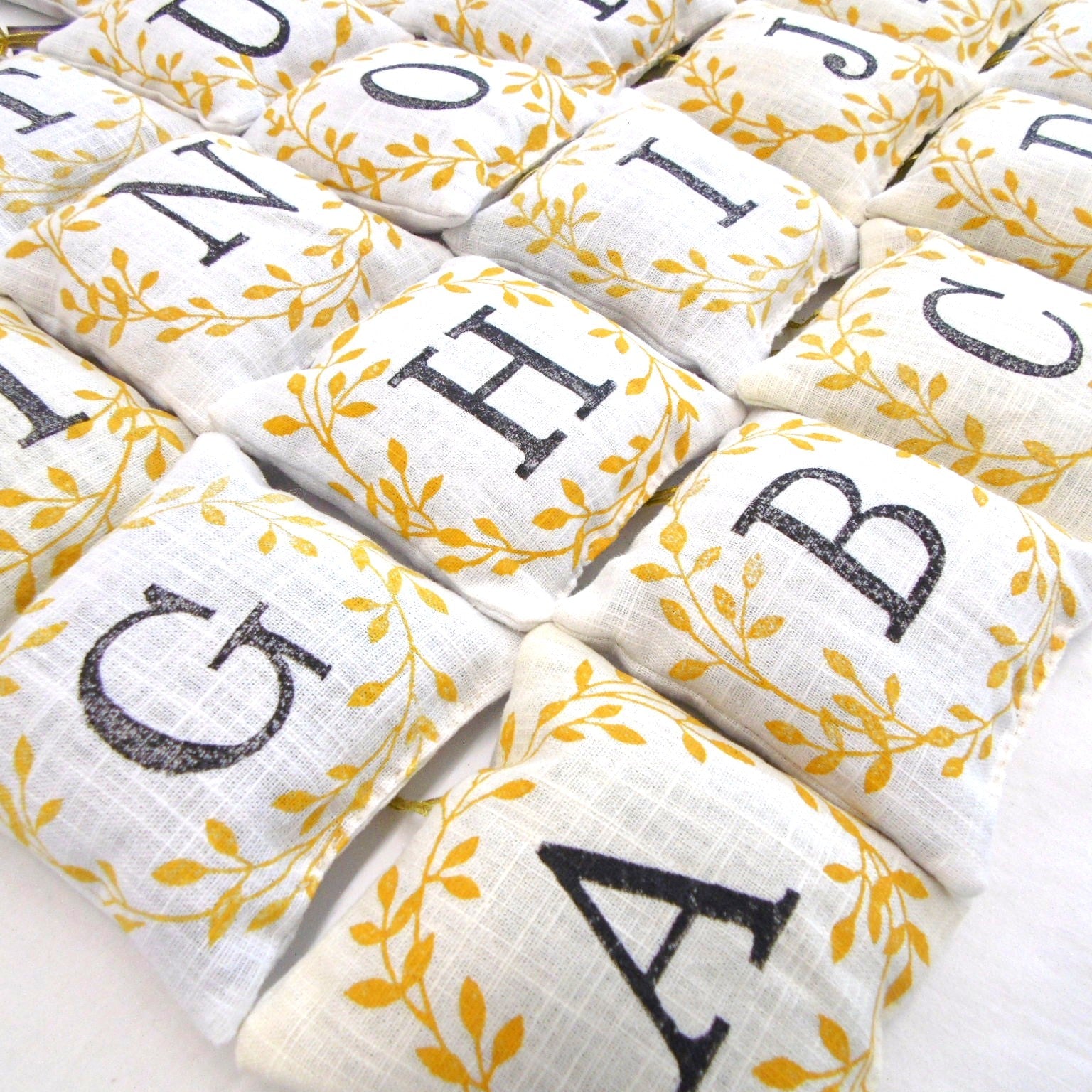Collection of hand block printed alphabet lavender sachets with golden leaf design showing letters G H B C and more, by Naila Ahmad London