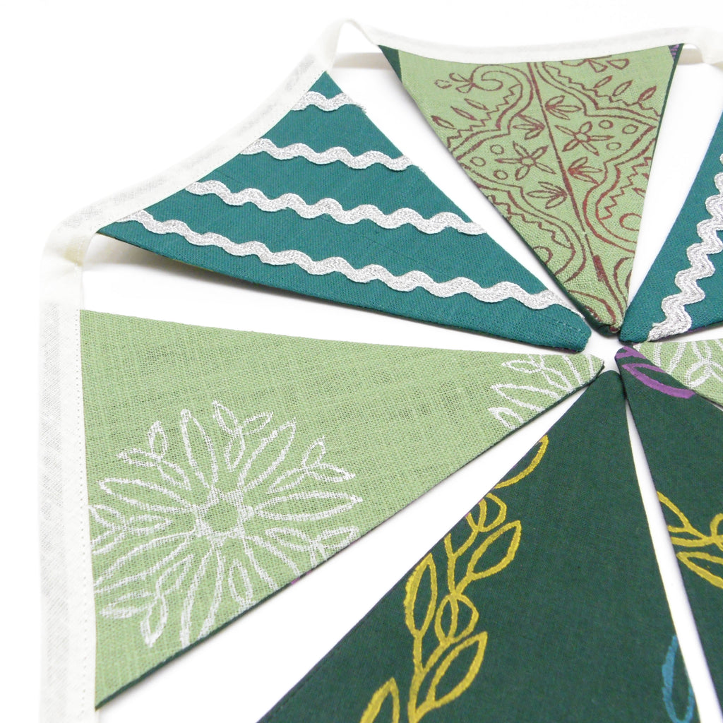Close up of sage green and teal hand block printed bunting flags with silver ricrac trim and floral motifs