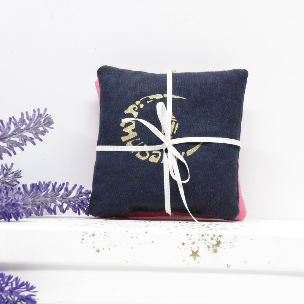 Navy blue pillow with gold design and white ribbon on a white surface with lavender.