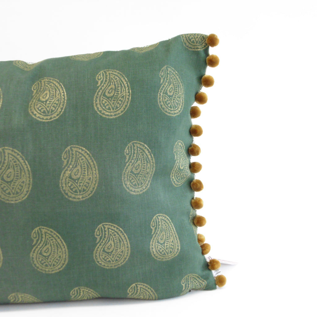 Green pillow with paisley pattern and pom-pom trim on a white background