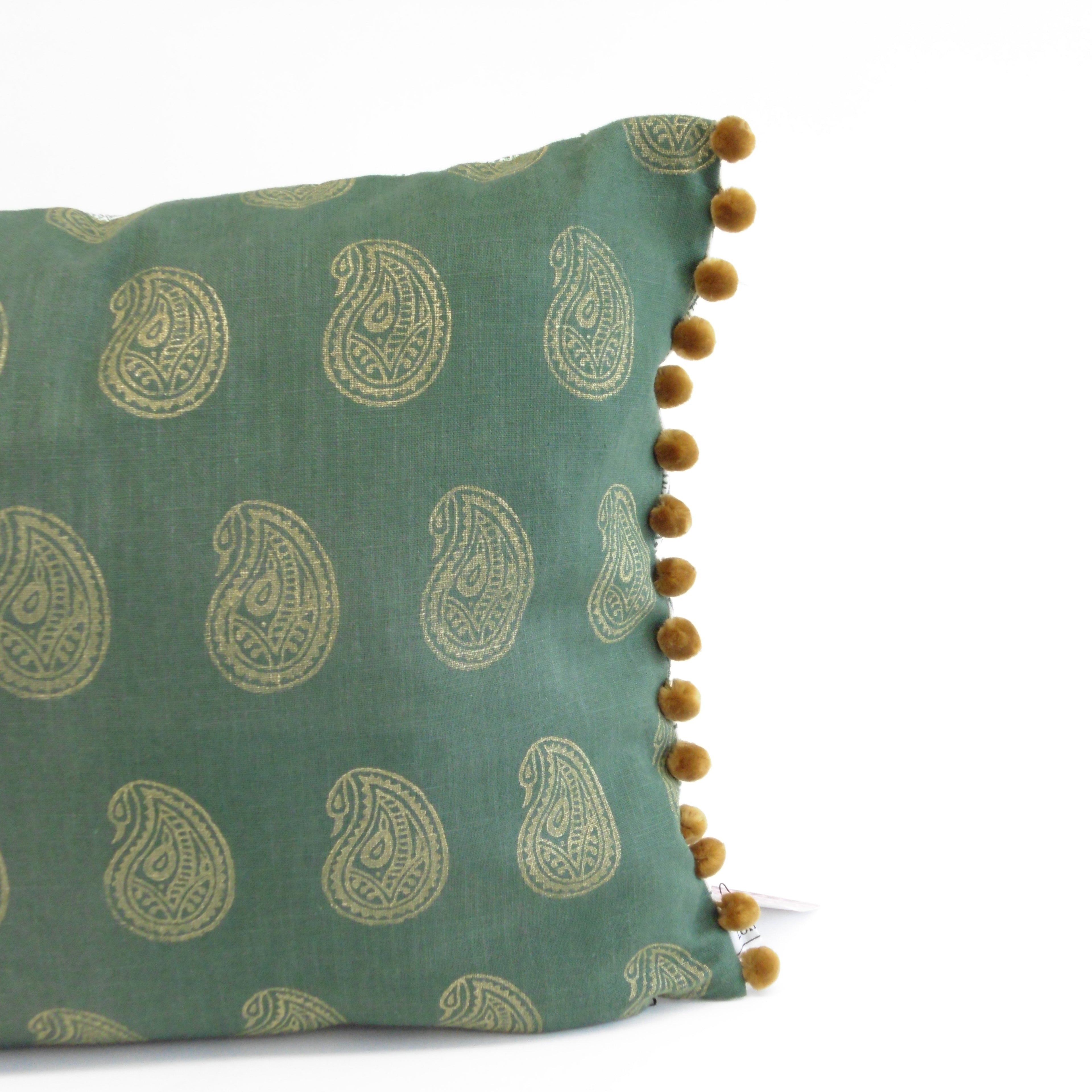 Green pillow with paisley pattern and pom-pom trim on a white background
