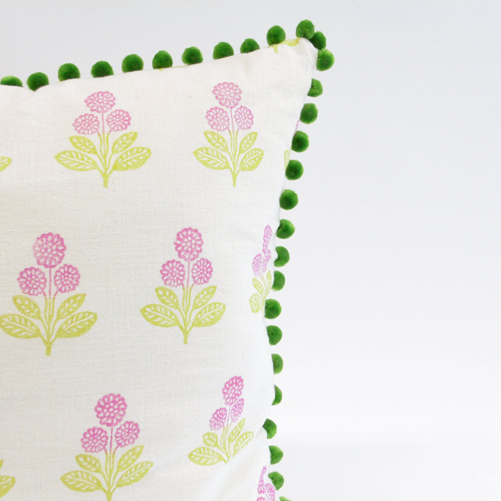 Decorative pillow with floral patterns and green pom-pom trim on a white background