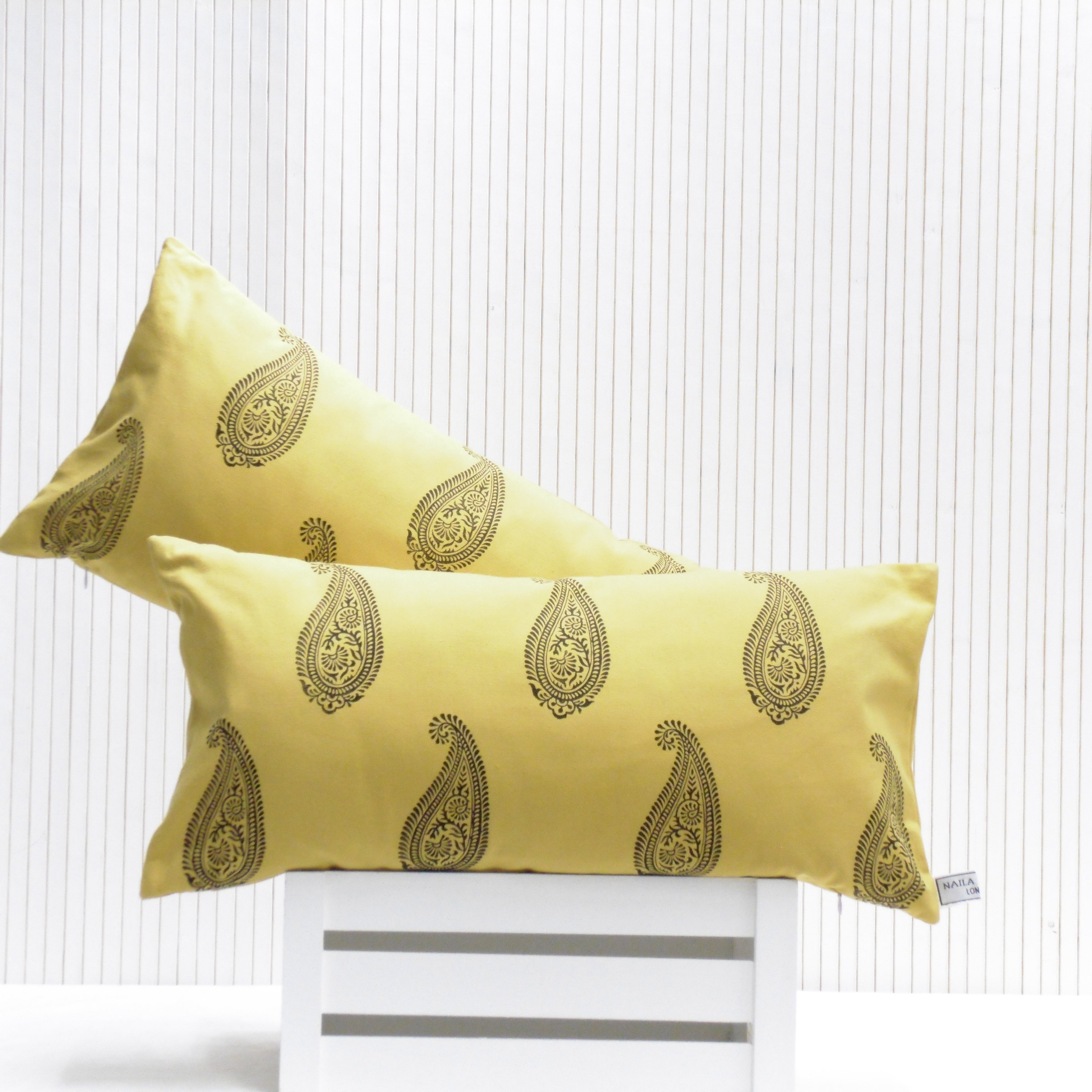 Two yellow pillows with black patterns on a white chair against a white background