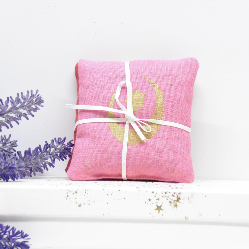 Pink fabric package with white ribbon on a white surface with lavender flowers.