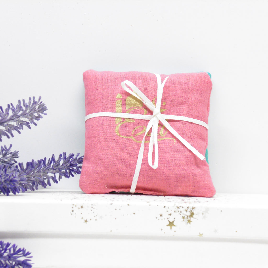 Pink fabric pouch with white drawstring on a white background with lavender leaves.