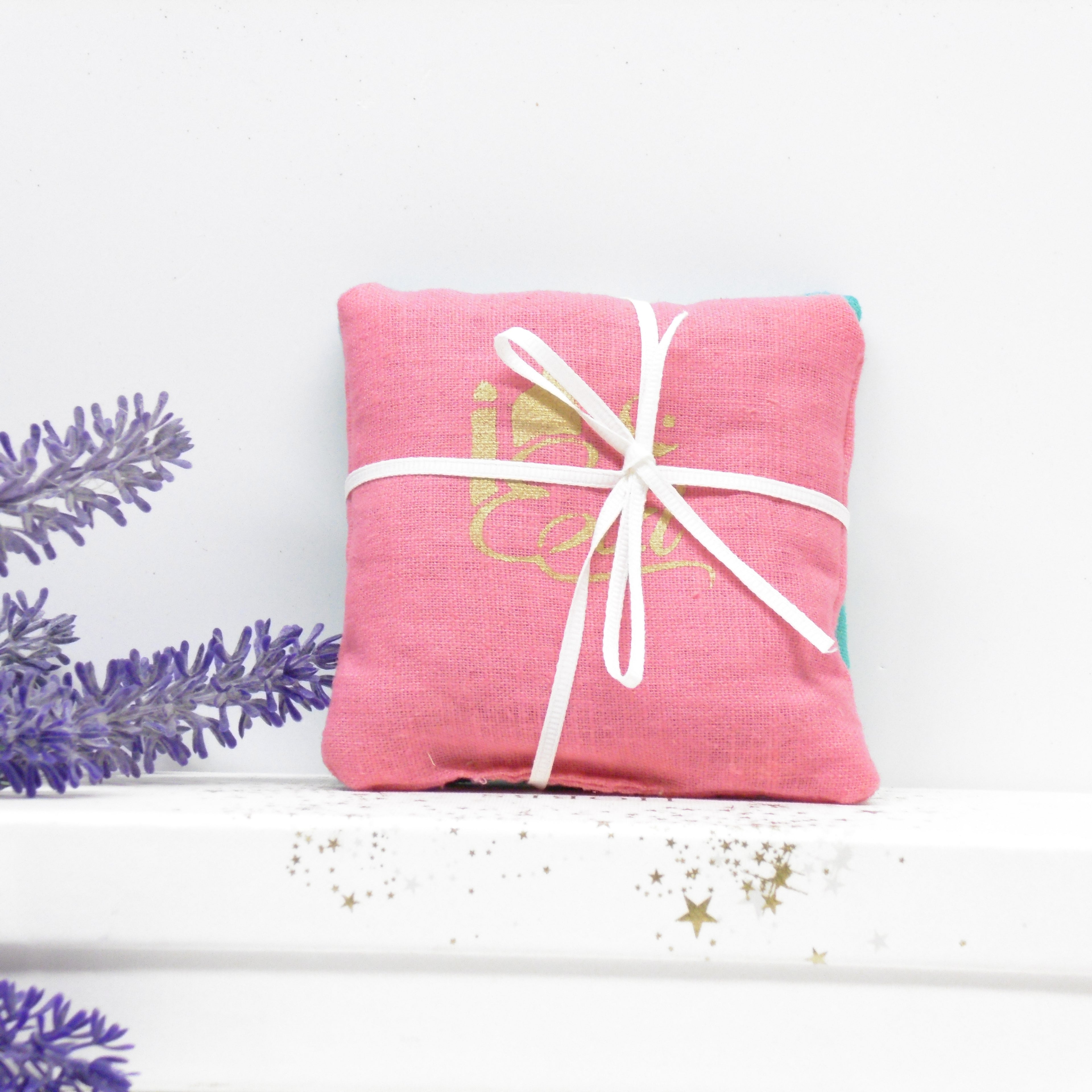 Pink fabric pouch with white drawstring on a white background with lavender leaves.