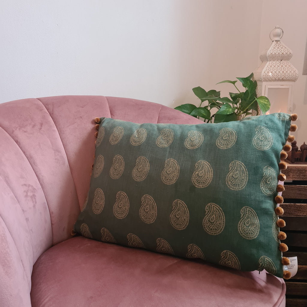 Green patterned pillow on a pink couch with a plant in the background
