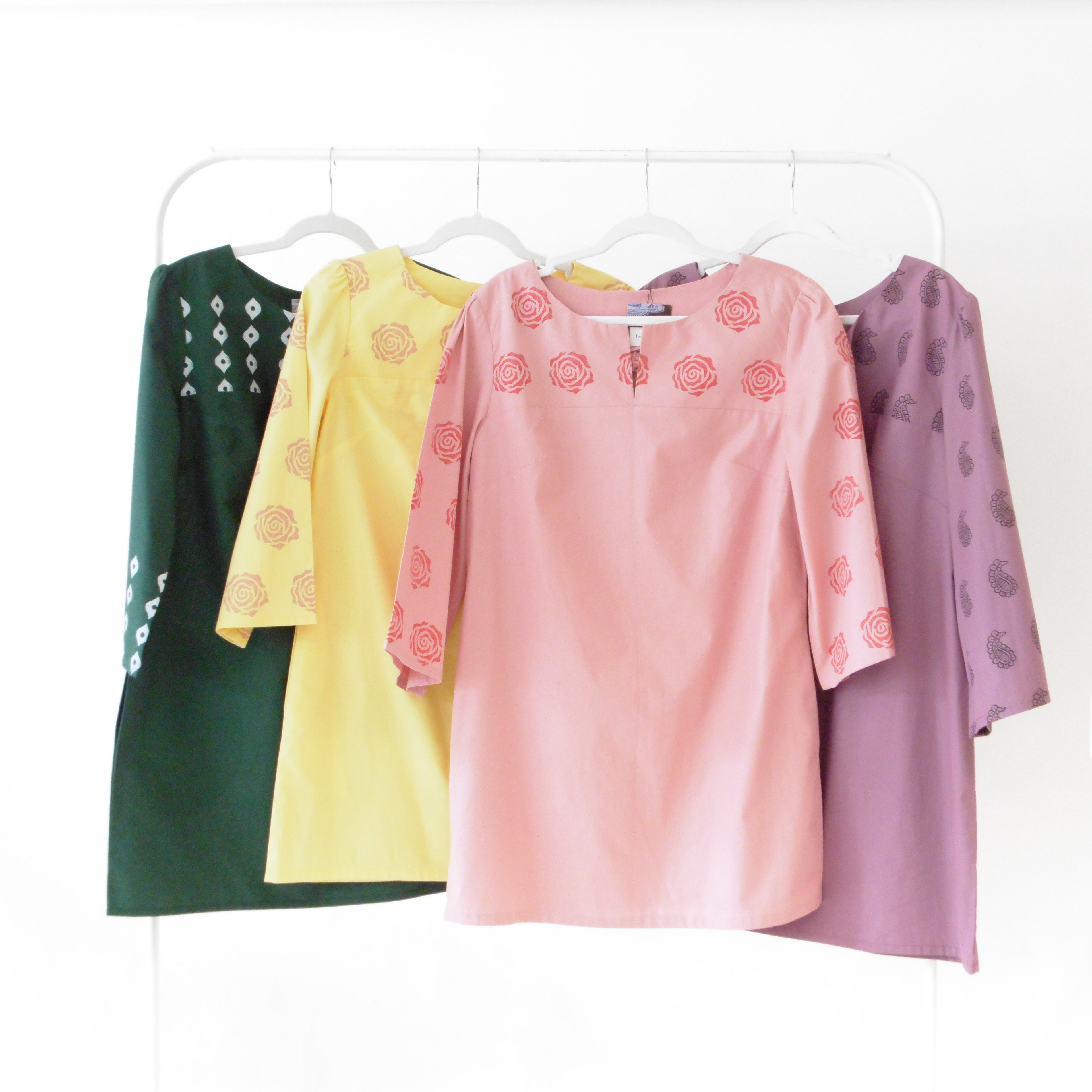 Four colorful tops on hangers against a white background