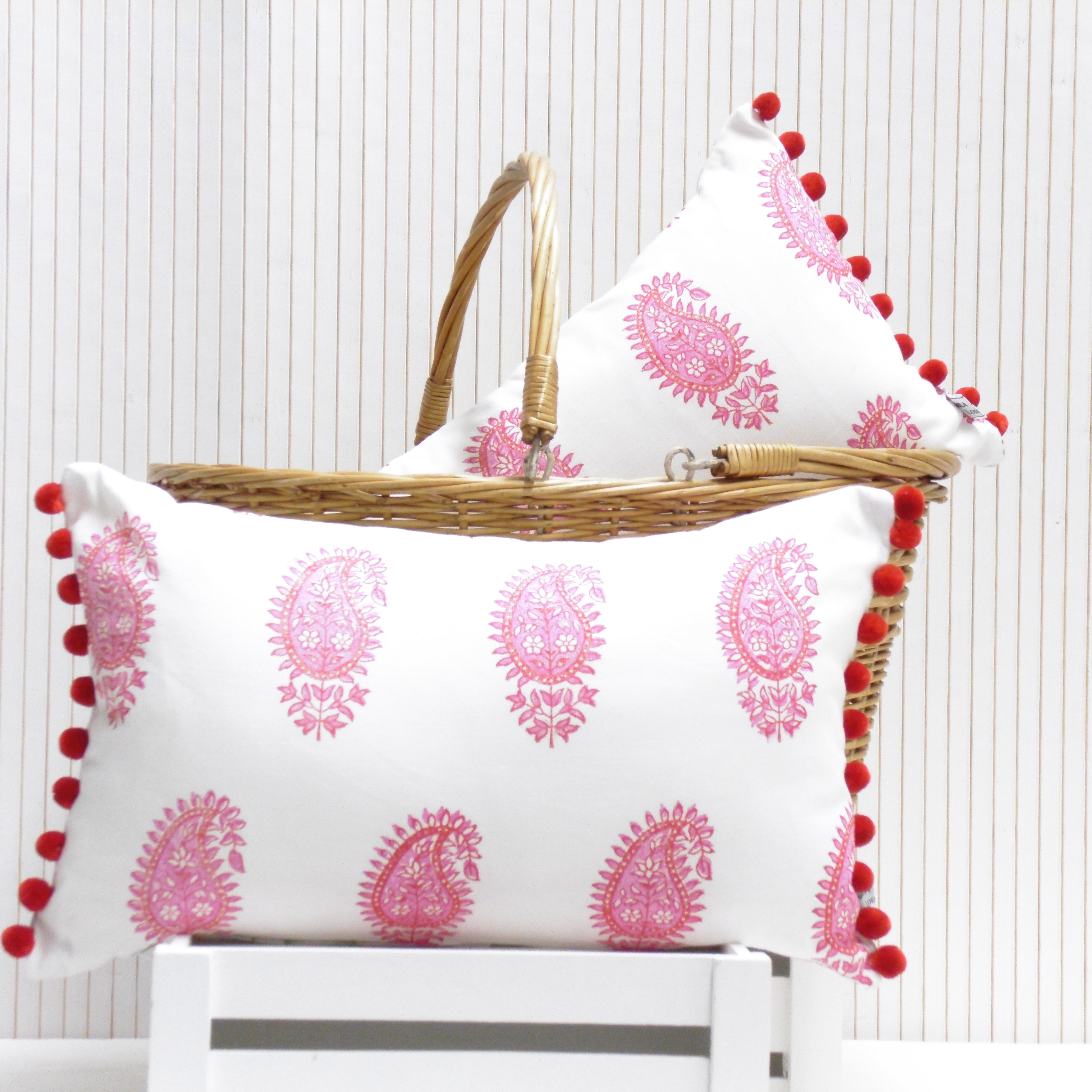 White pillows with pink patterns and red pom-poms on a white surface