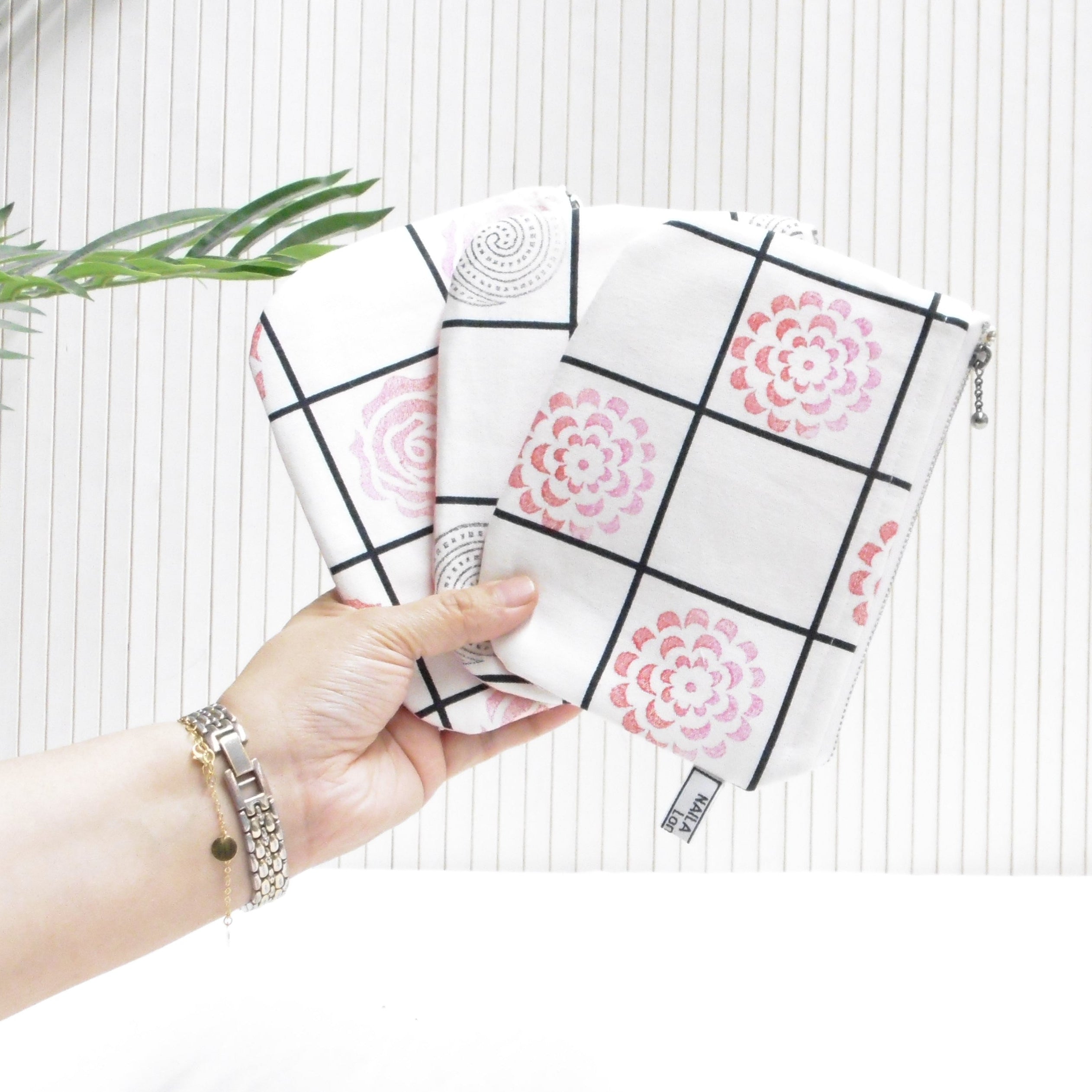 Hand holding a patterned pouch against a white background with green leaves on the side.
