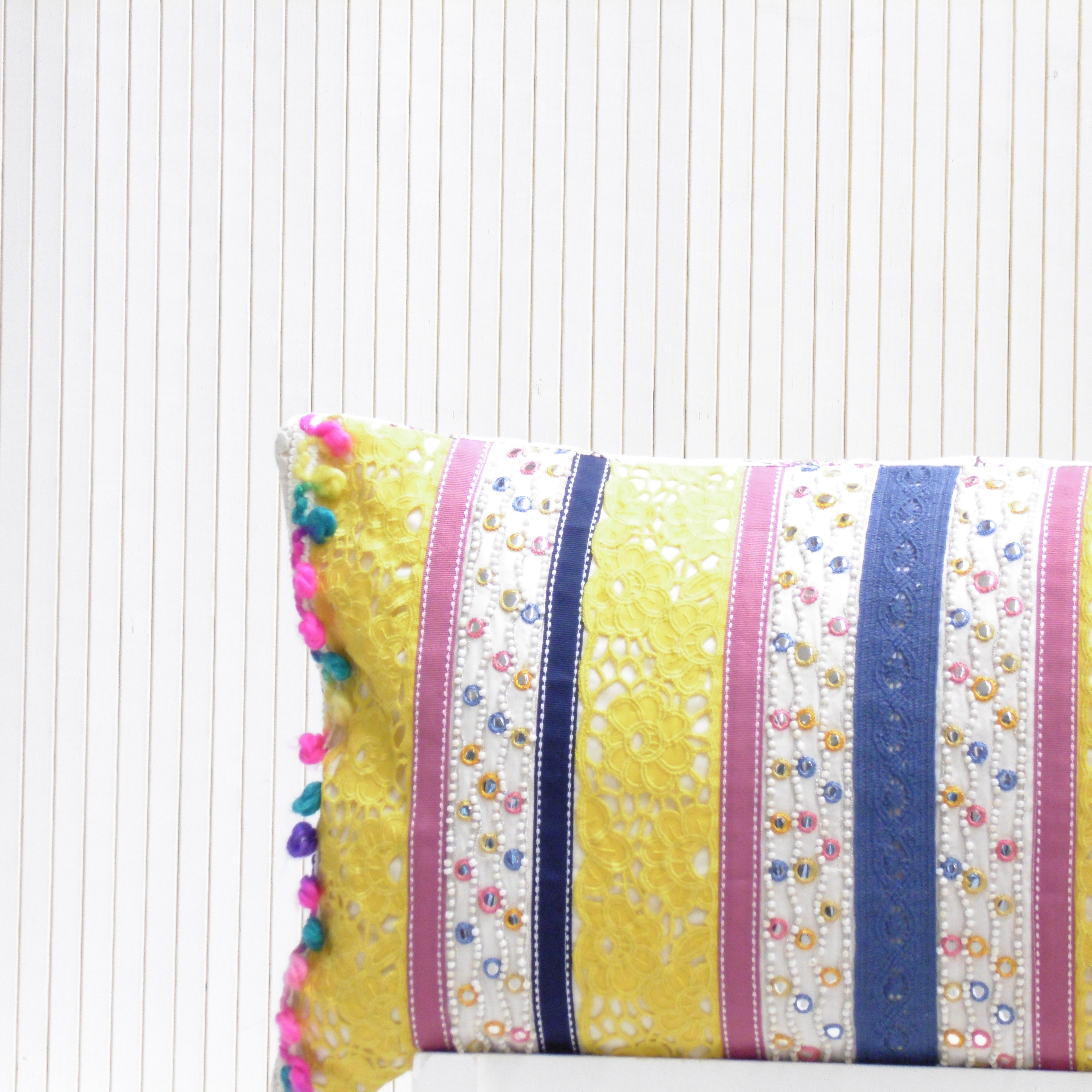 Colorful striped pillow with pom-pom trim on a white background