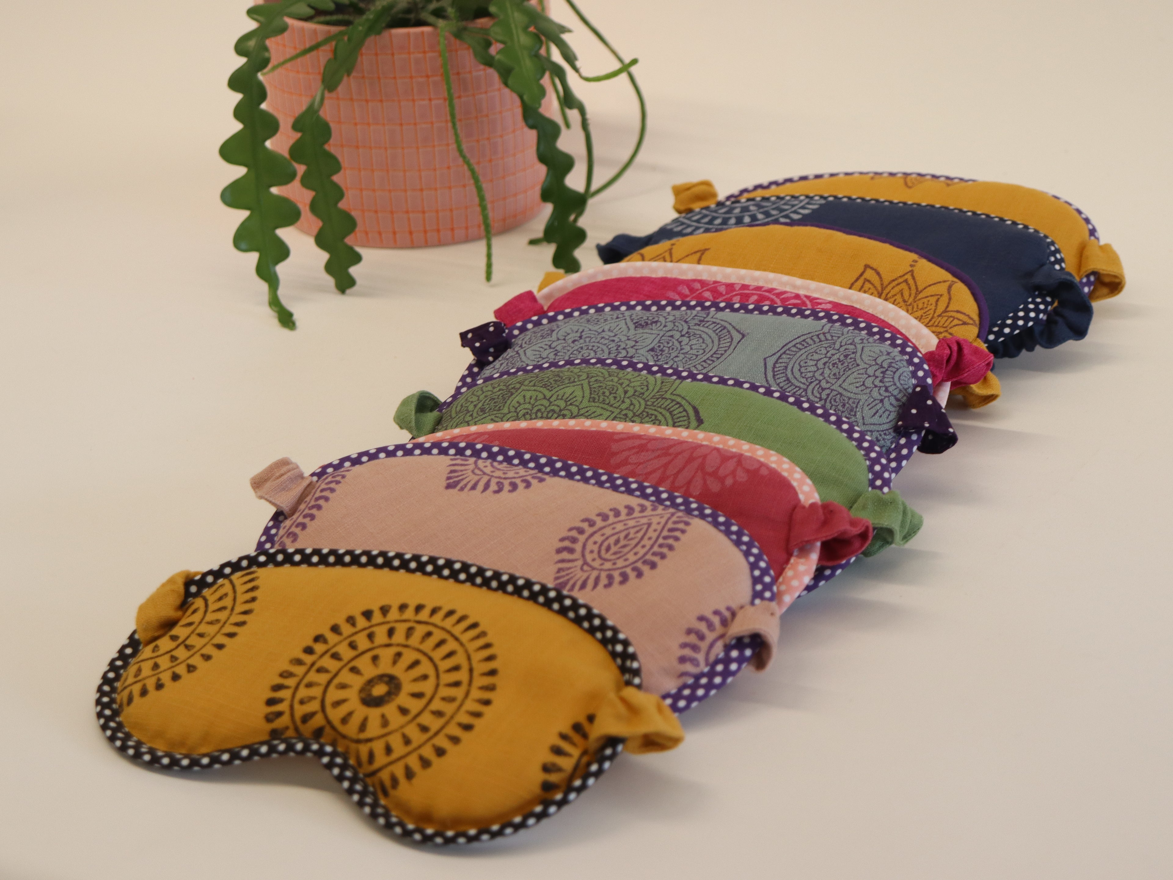 Colorful embroidered eye pillows arranged on a light surface with a plant in the background.