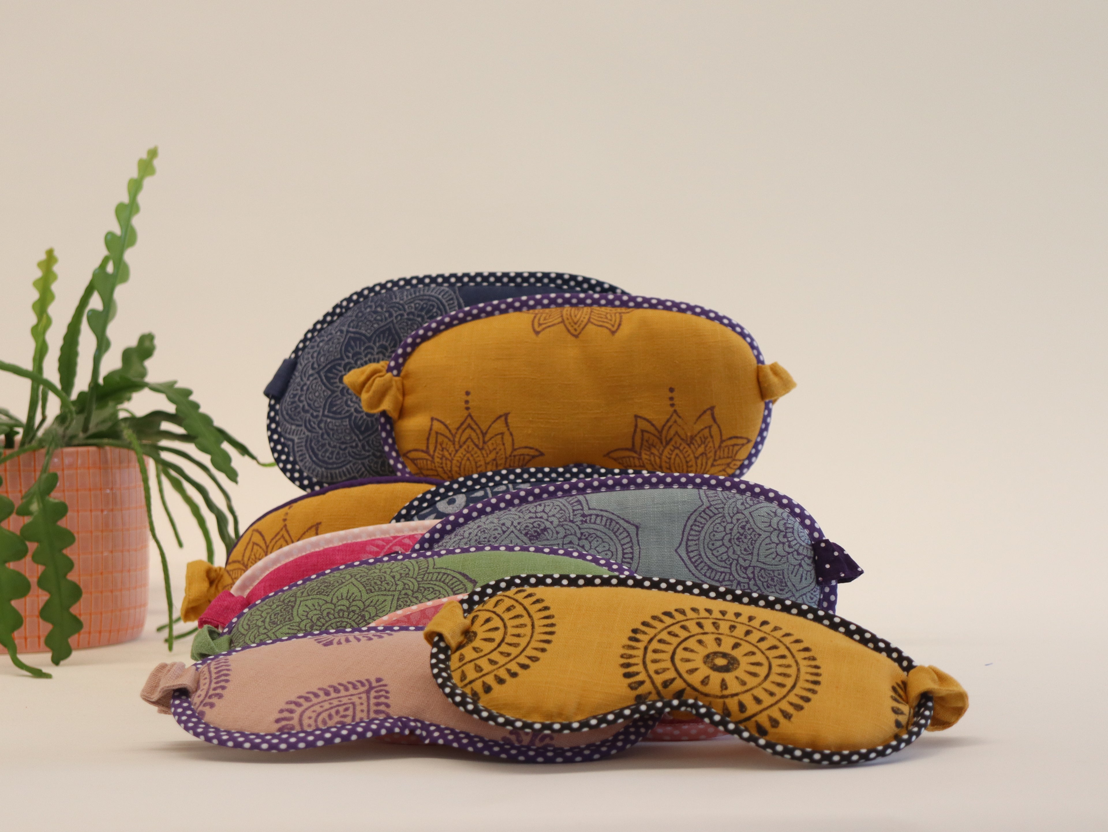 Stack of colorful fabric eye pillows on a neutral background with a plant.