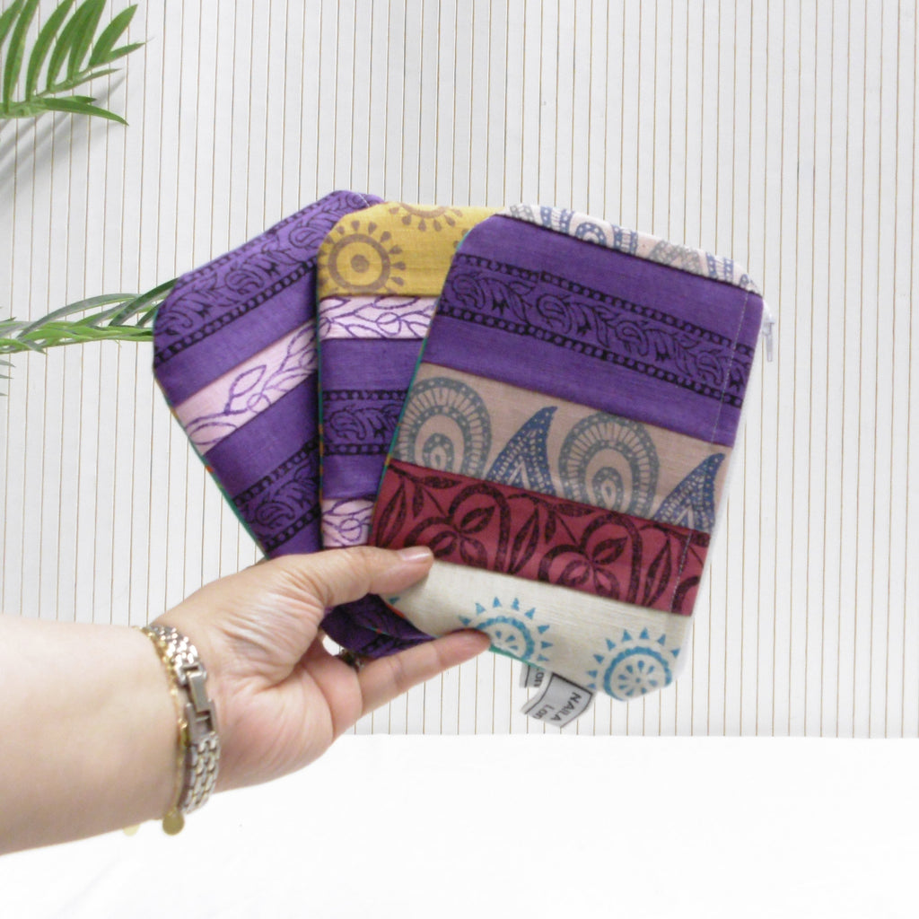 Hand holding a stack of colorful fabric swatches against a white background with green leaves.