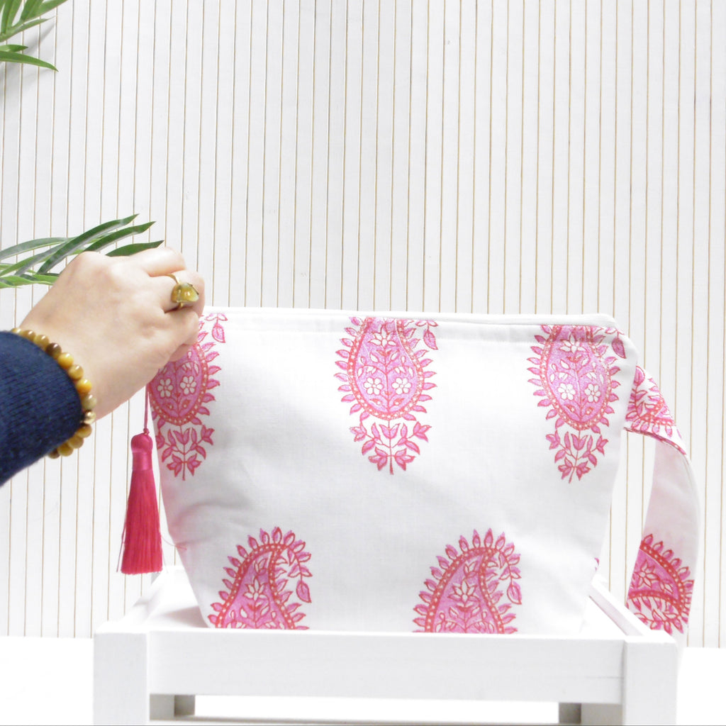 Hand holding a white pouch with pink patterns and a red tassel against a white background