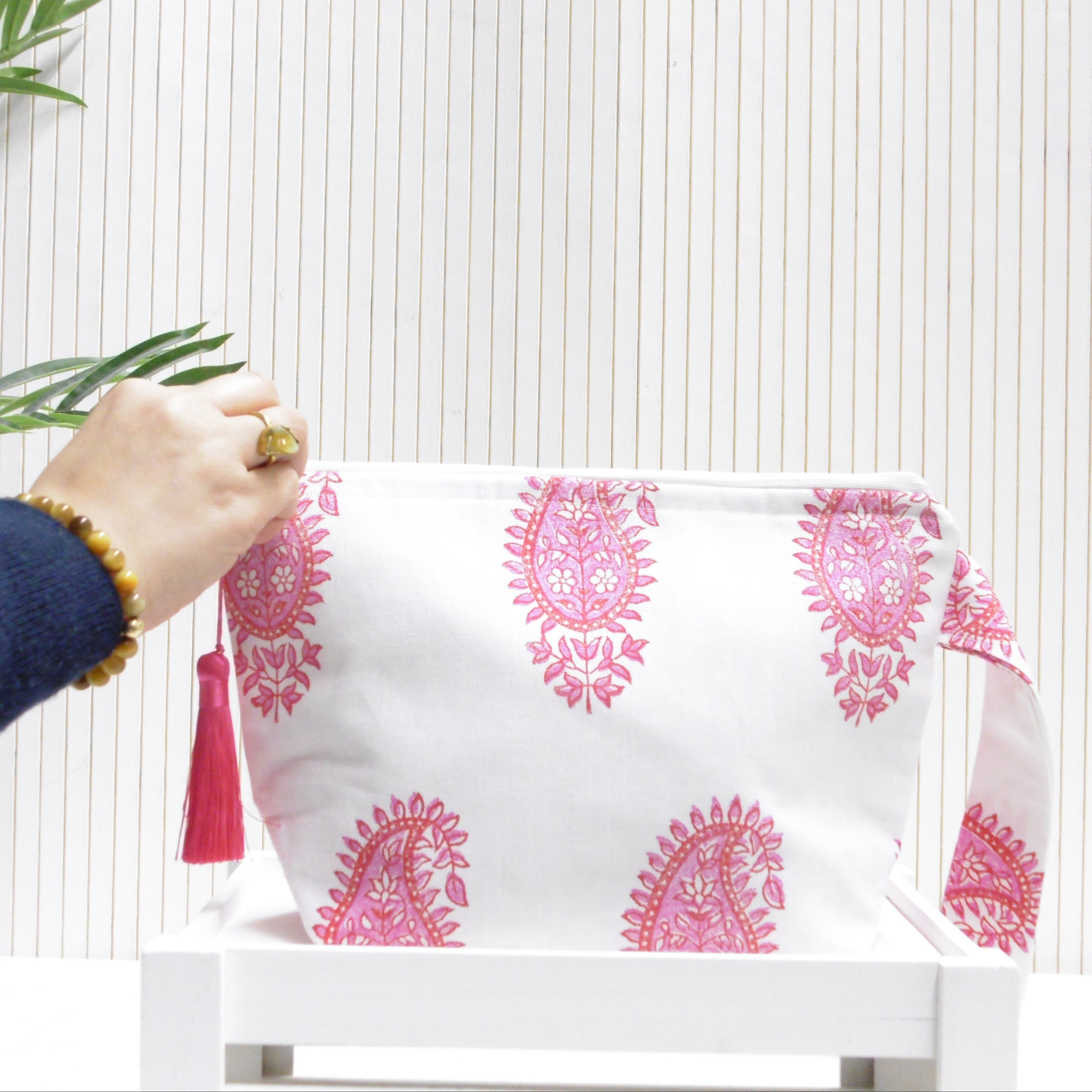 Hand holding a white pouch with pink patterns and a red tassel against a white background