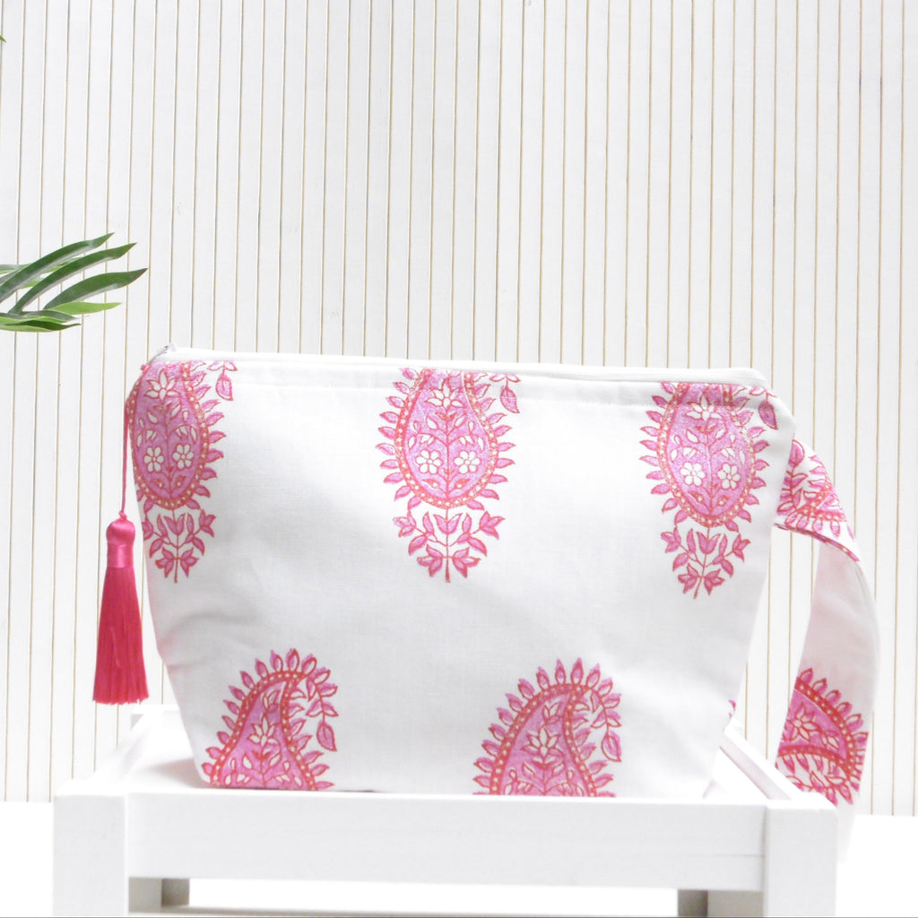 White pouch with pink paisley patterns and a tassel on a white surface with a light background