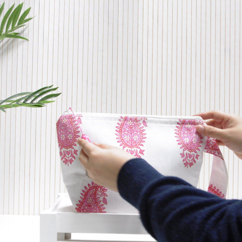 Person holding a white pouch with pink floral patterns against a white background