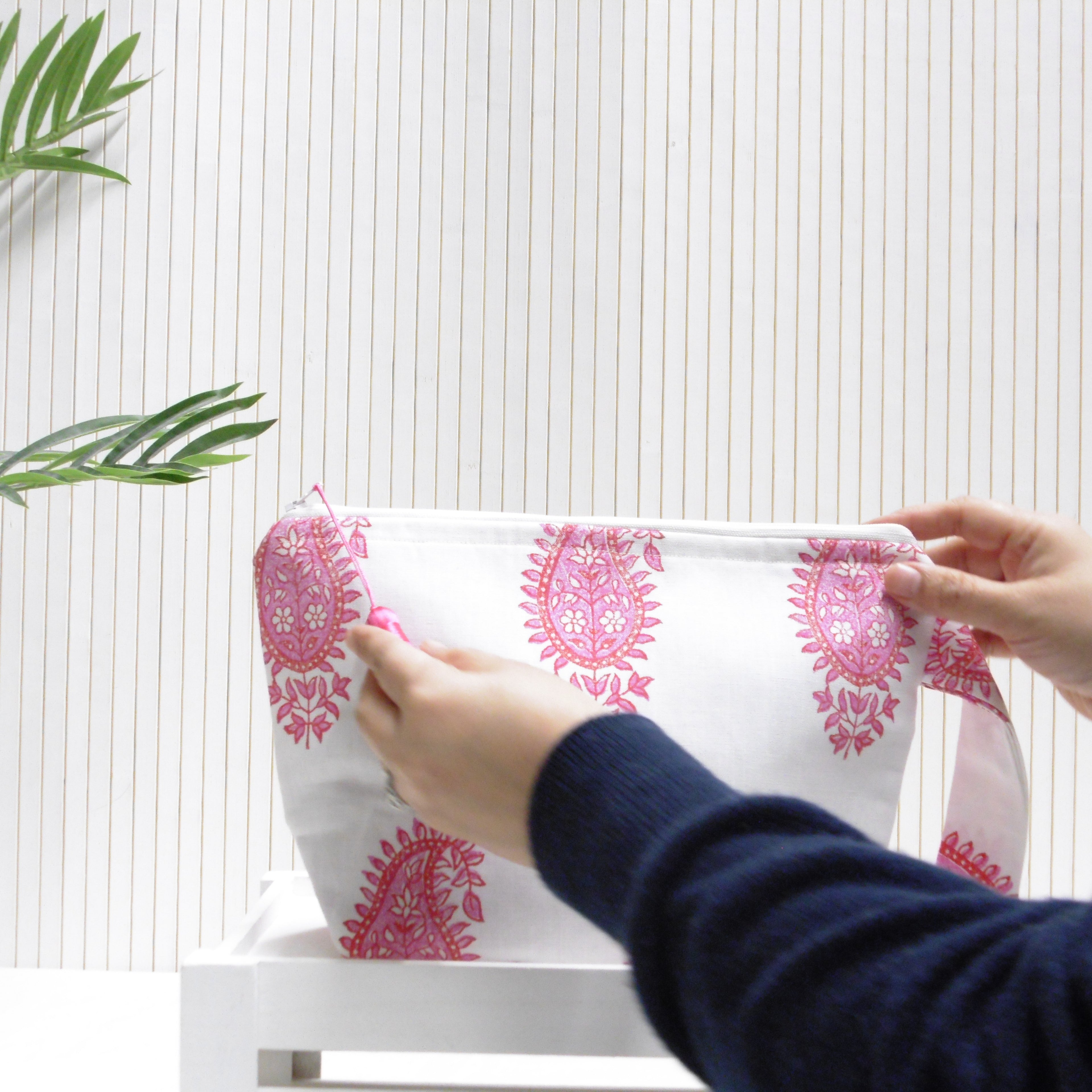 Person holding a white pouch with pink floral patterns against a white background