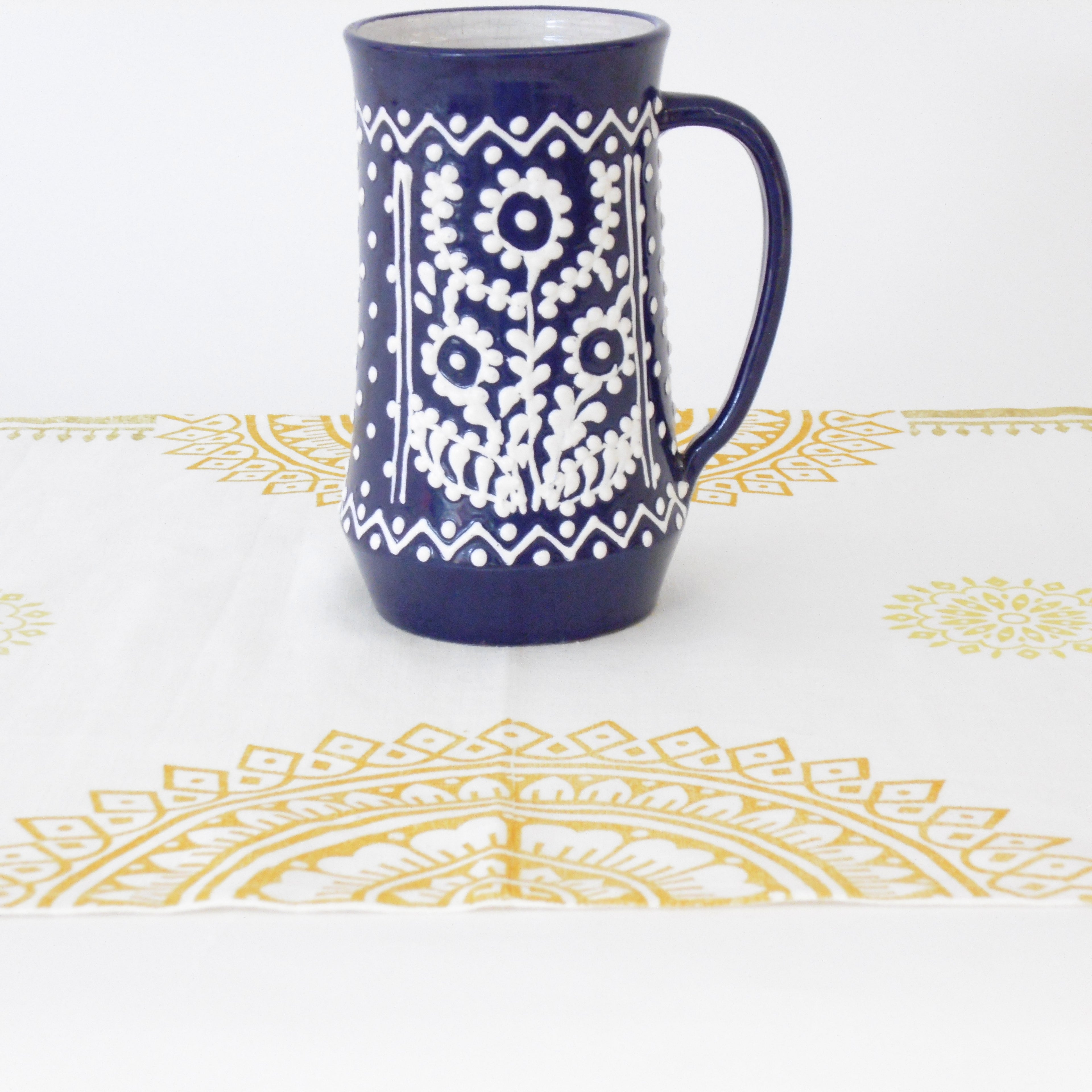 Navy blue mug with white floral pattern on a white background with gold decorative elements.