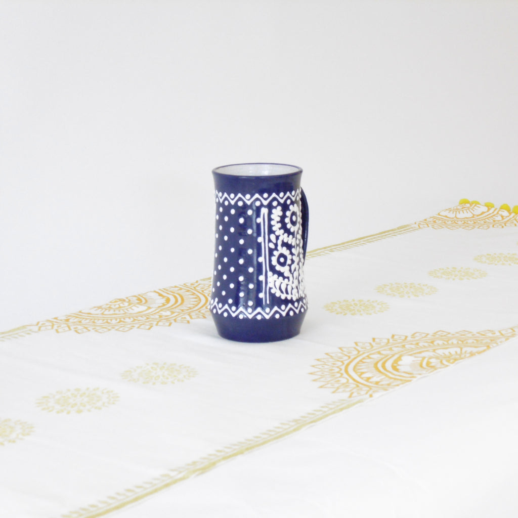 Blue mug with white patterns on a white tablecloth with gold designs