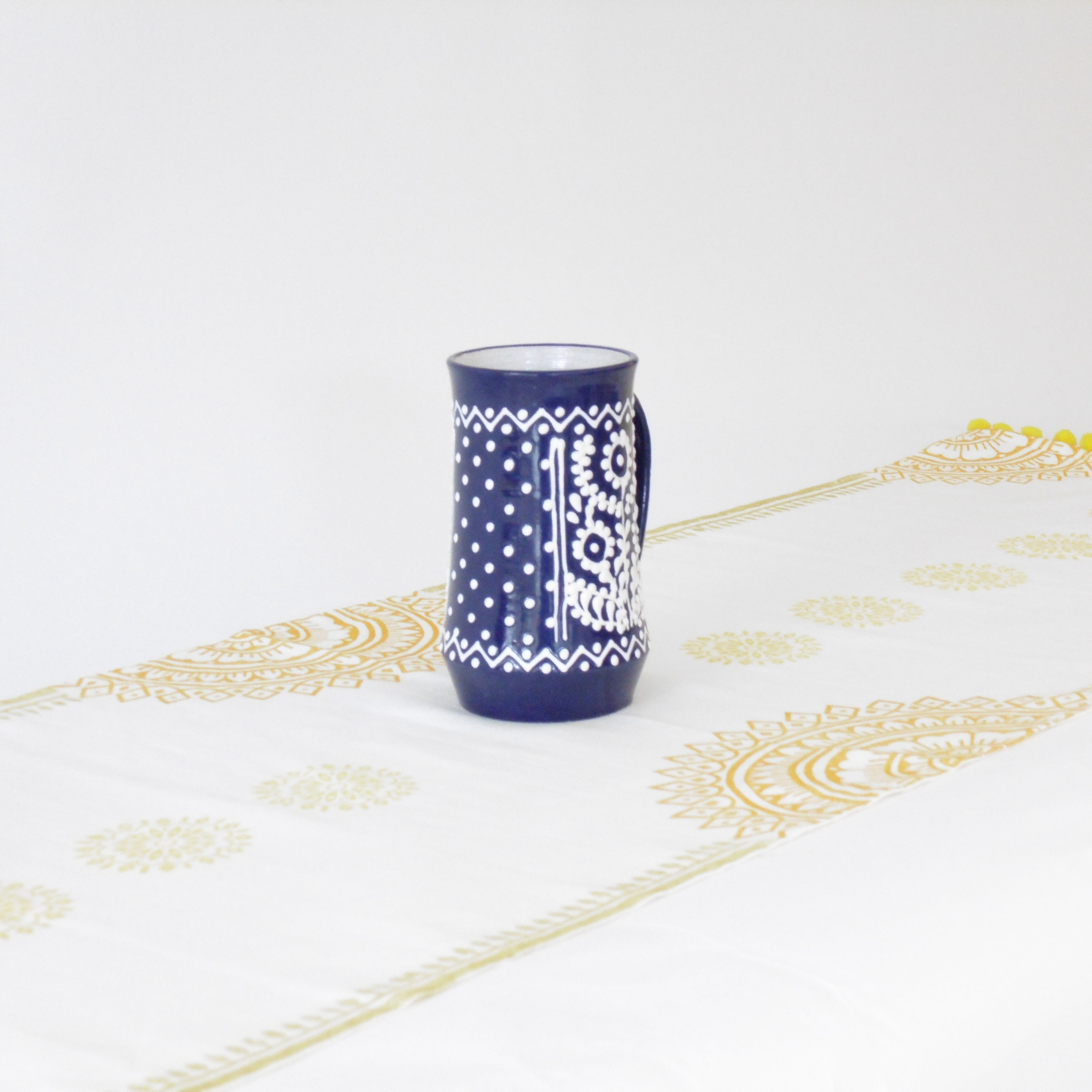 Blue mug with white patterns on a white tablecloth with gold designs