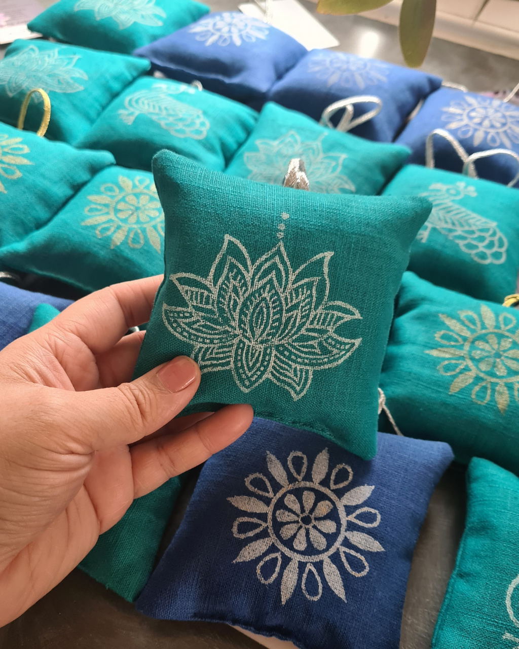 Teal fabric pouch with white floral design held by a hand, surrounded by similar pouches.