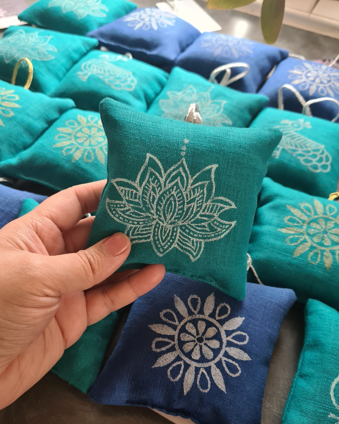Teal fabric pouch with white floral design held by a hand, surrounded by similar pouches.