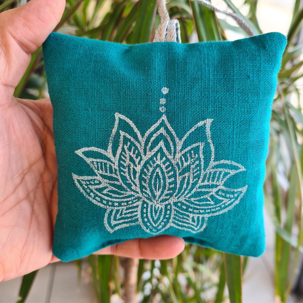 Teal fabric pouch with white lotus design held by a hand against a blurred green plant background