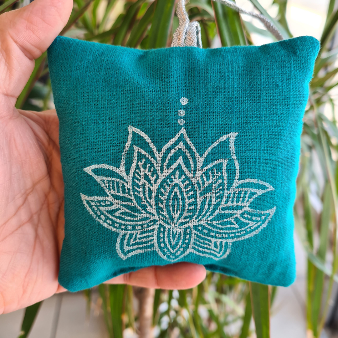 Teal fabric pouch with white lotus design held by a hand against a blurred green plant background