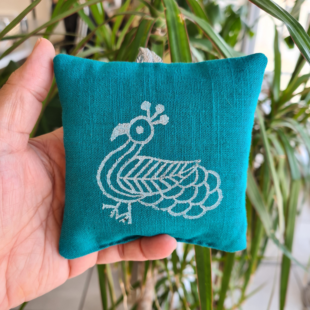 Teal fabric pouch with white bird design held in a hand against a plant background