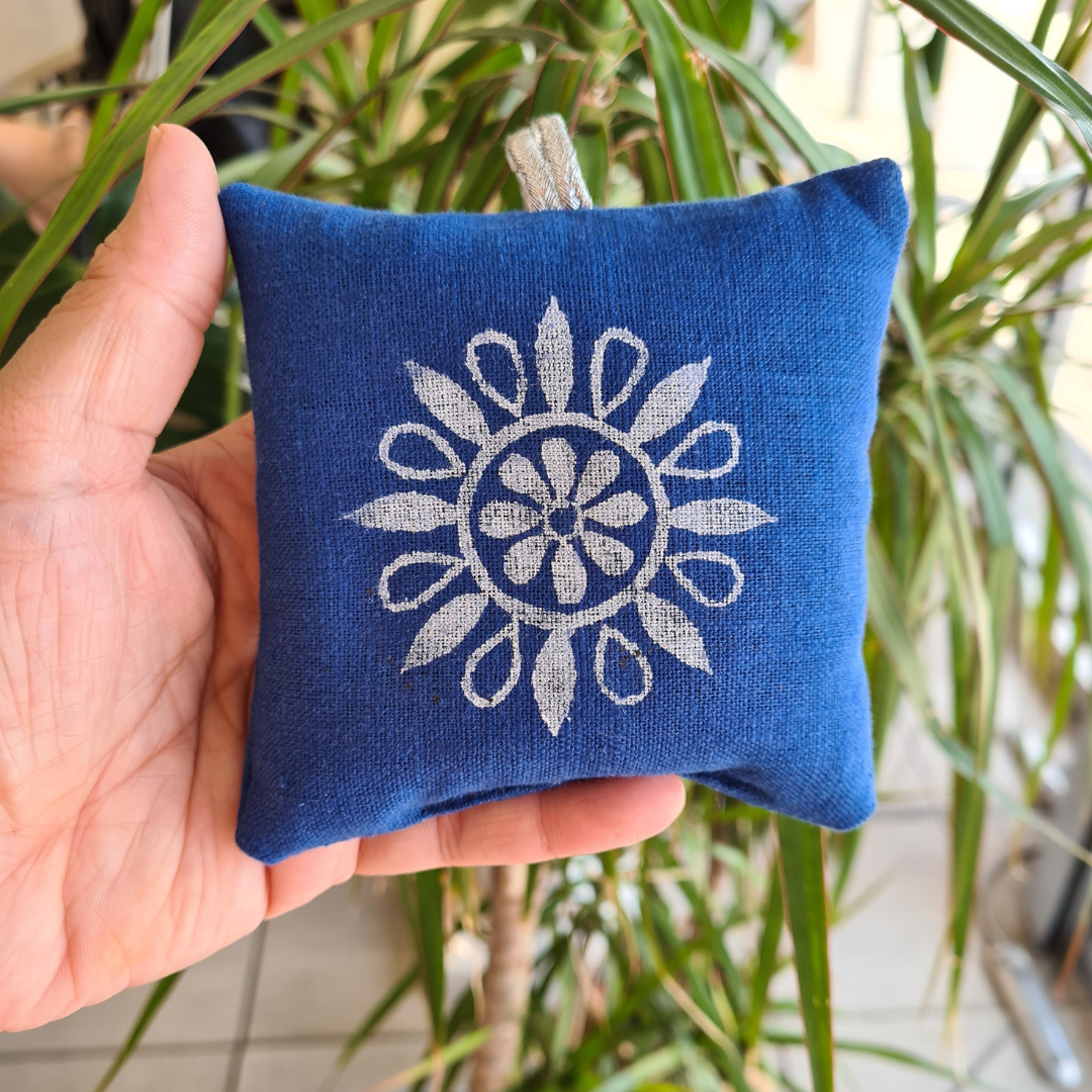 Blue fabric pouch with white floral design held in a hand against a plant background