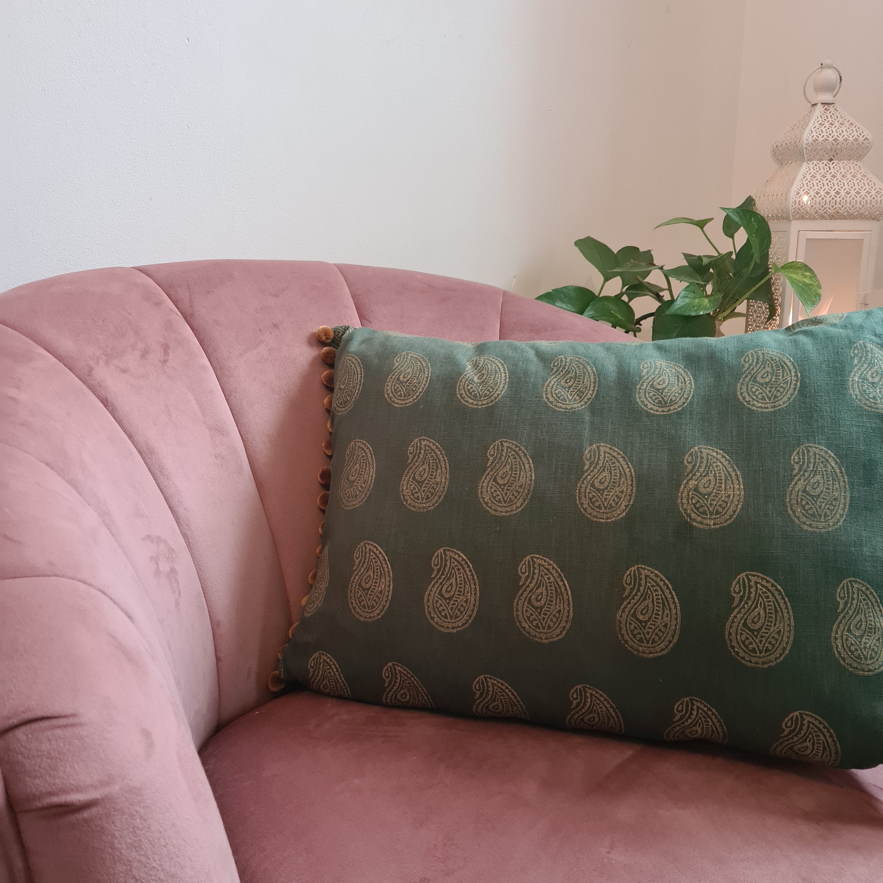 Green patterned pillow on a pink chair with a plant in the background