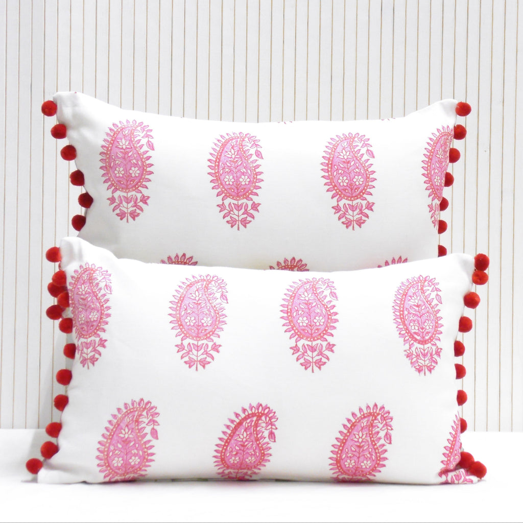 Two decorative pillows with pink patterns and red pom-poms on a white background