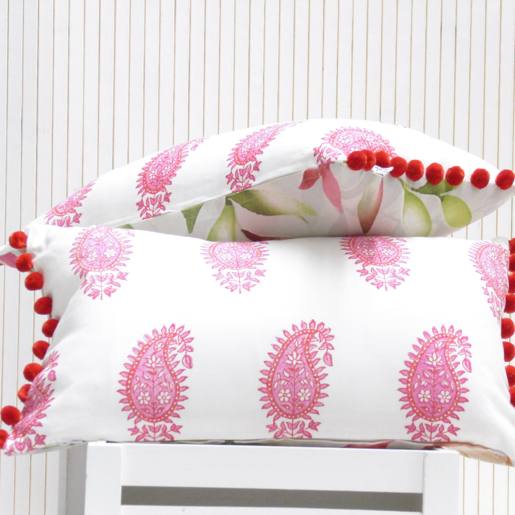 Two decorative pillows with pink patterns and red pom-poms on a white background