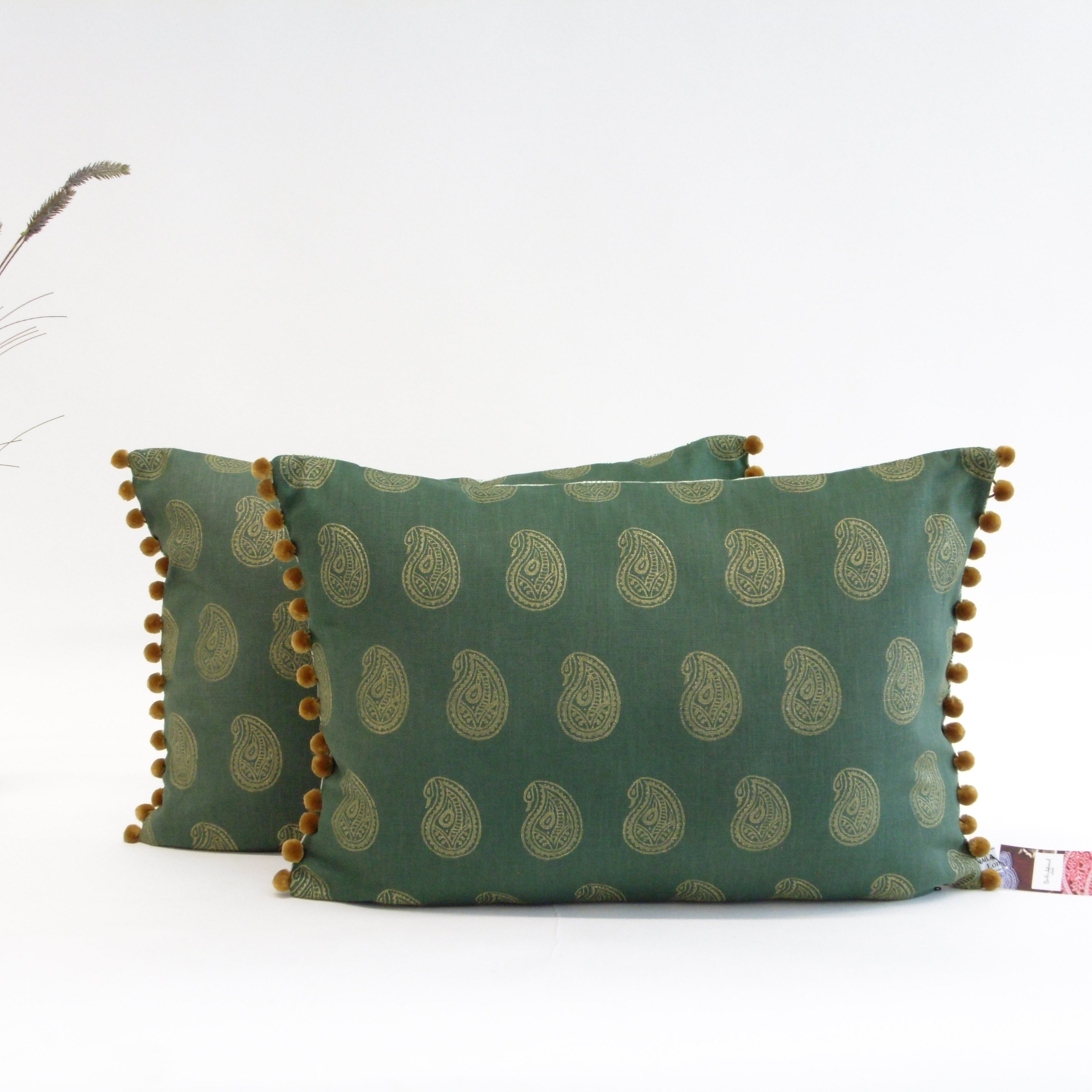 Green patterned pillow with pom-pom trim on a white background