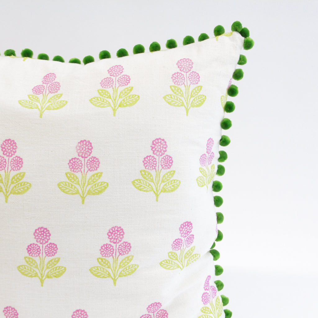 Decorative pillow with floral pattern and green pom-pom trim on a white background