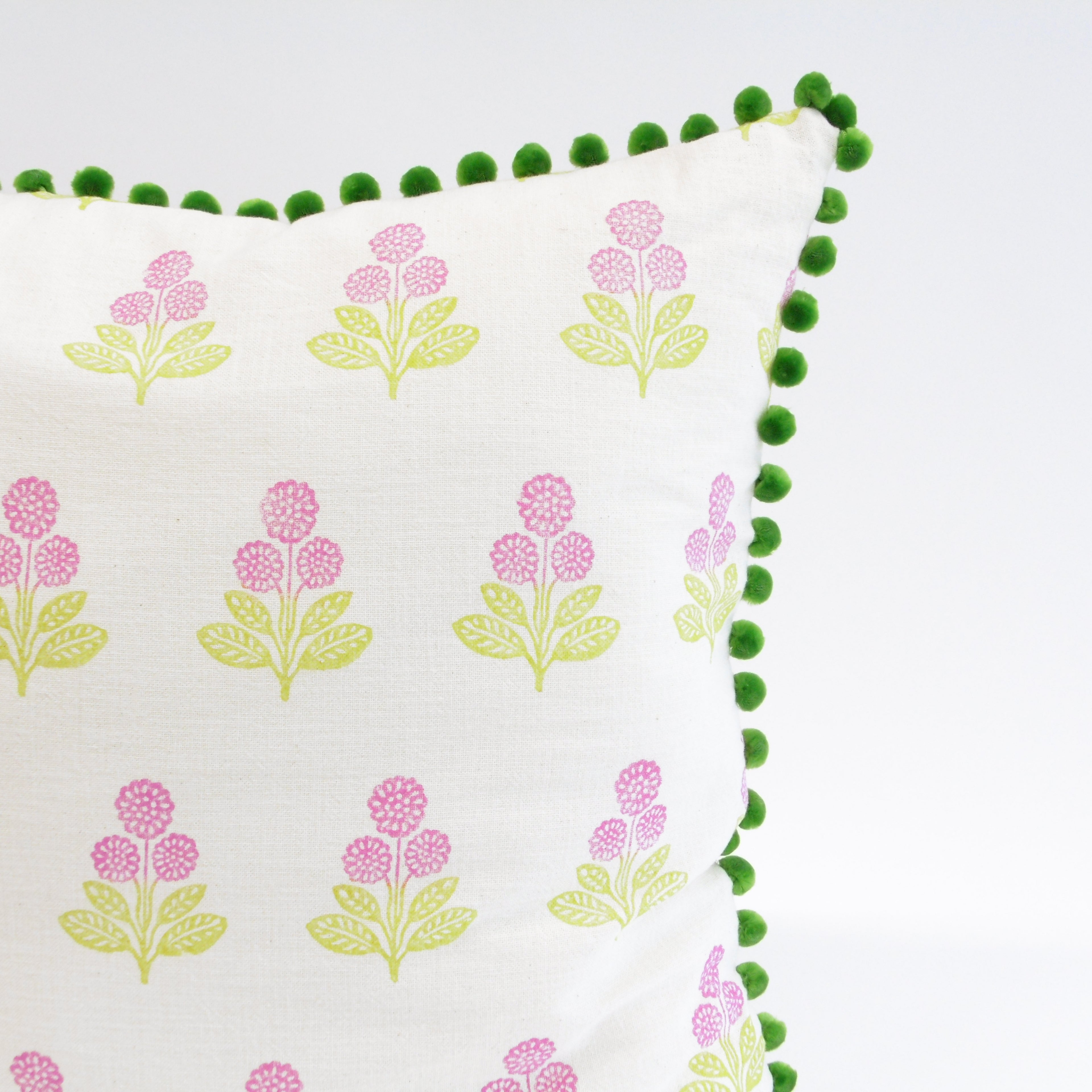 Decorative pillow with floral pattern and green pom-pom trim on a white background