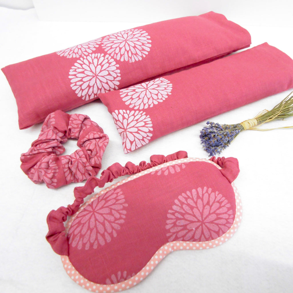 Pink eye mask, scrunchie, and pillow with floral pattern on a white background