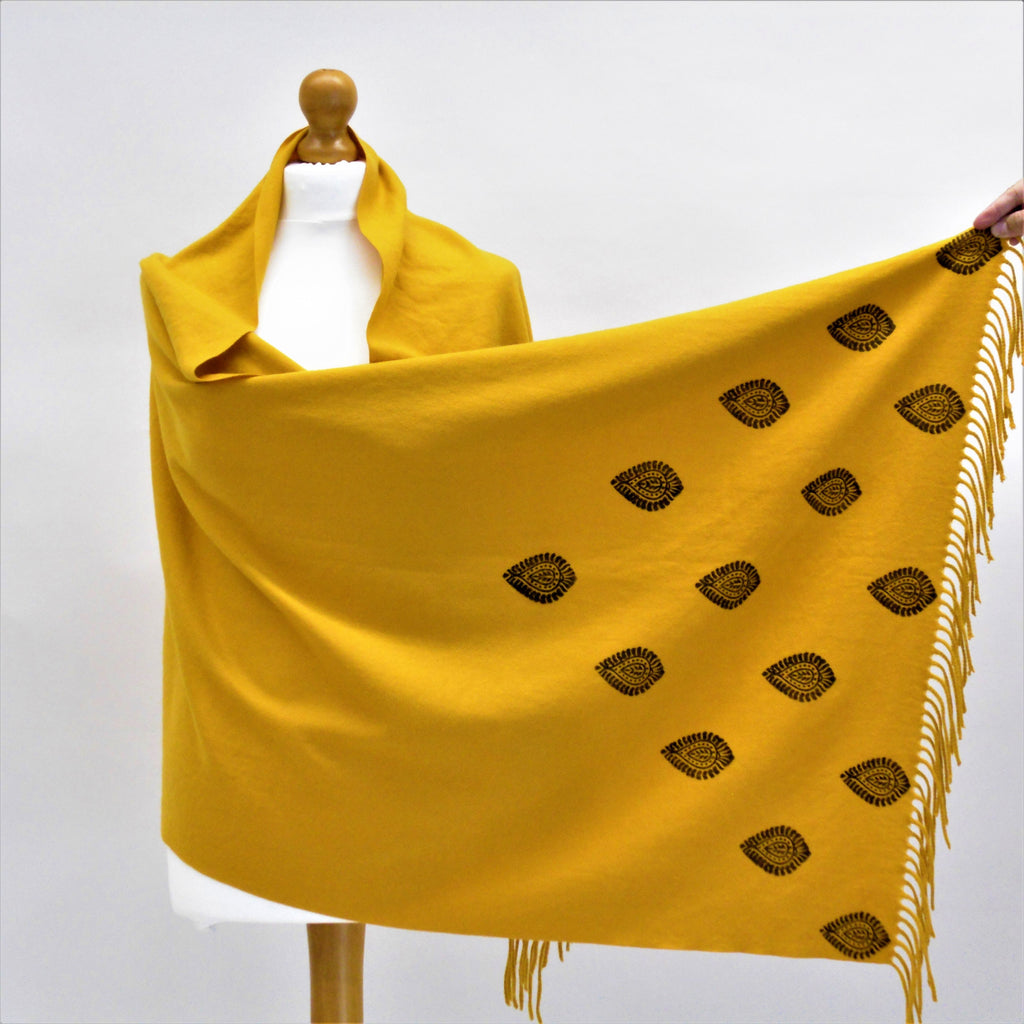 Yellow scarf with black patterns and fringes on a mannequin against a white background