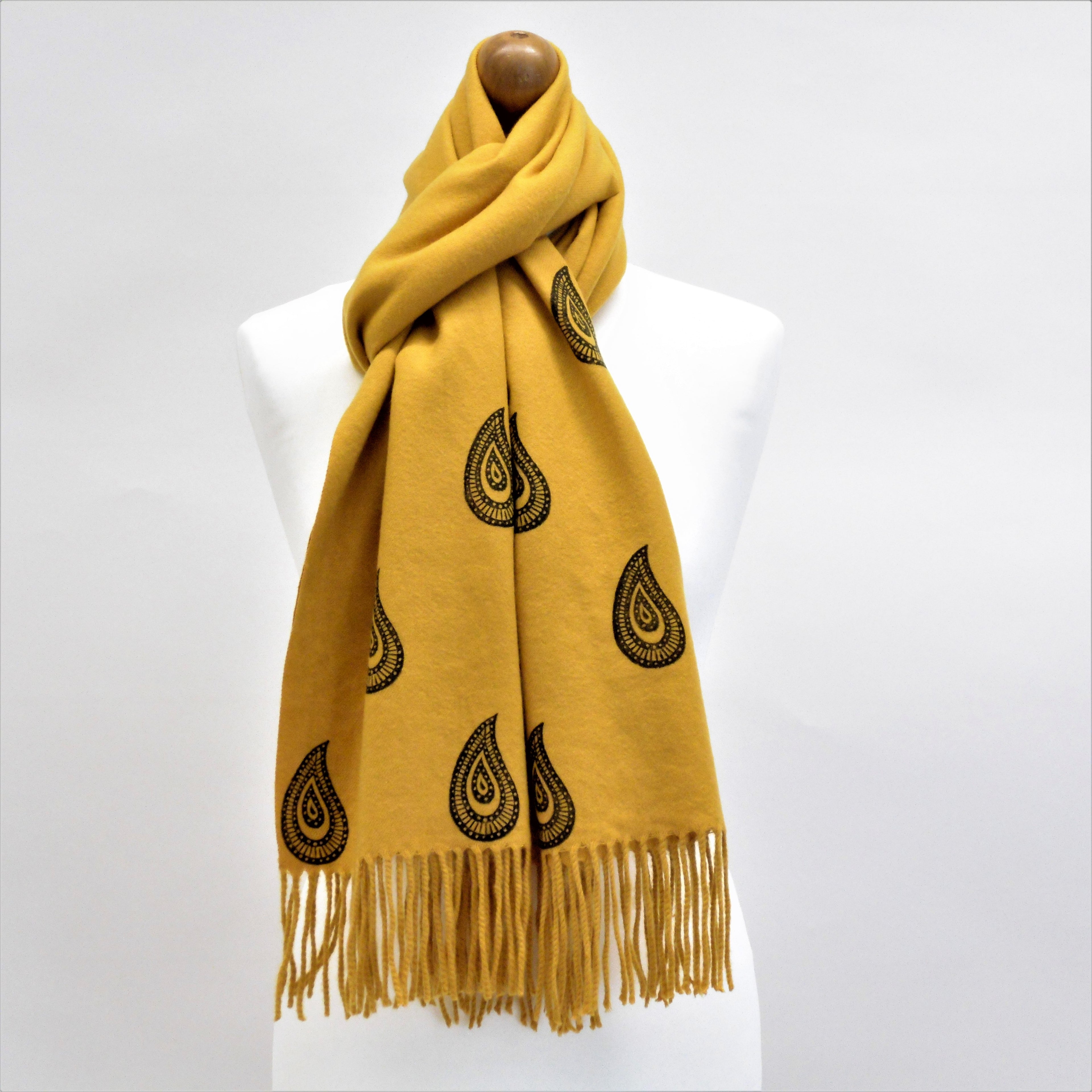 Yellow scarf with black patterns and fringes on a mannequin against a white background