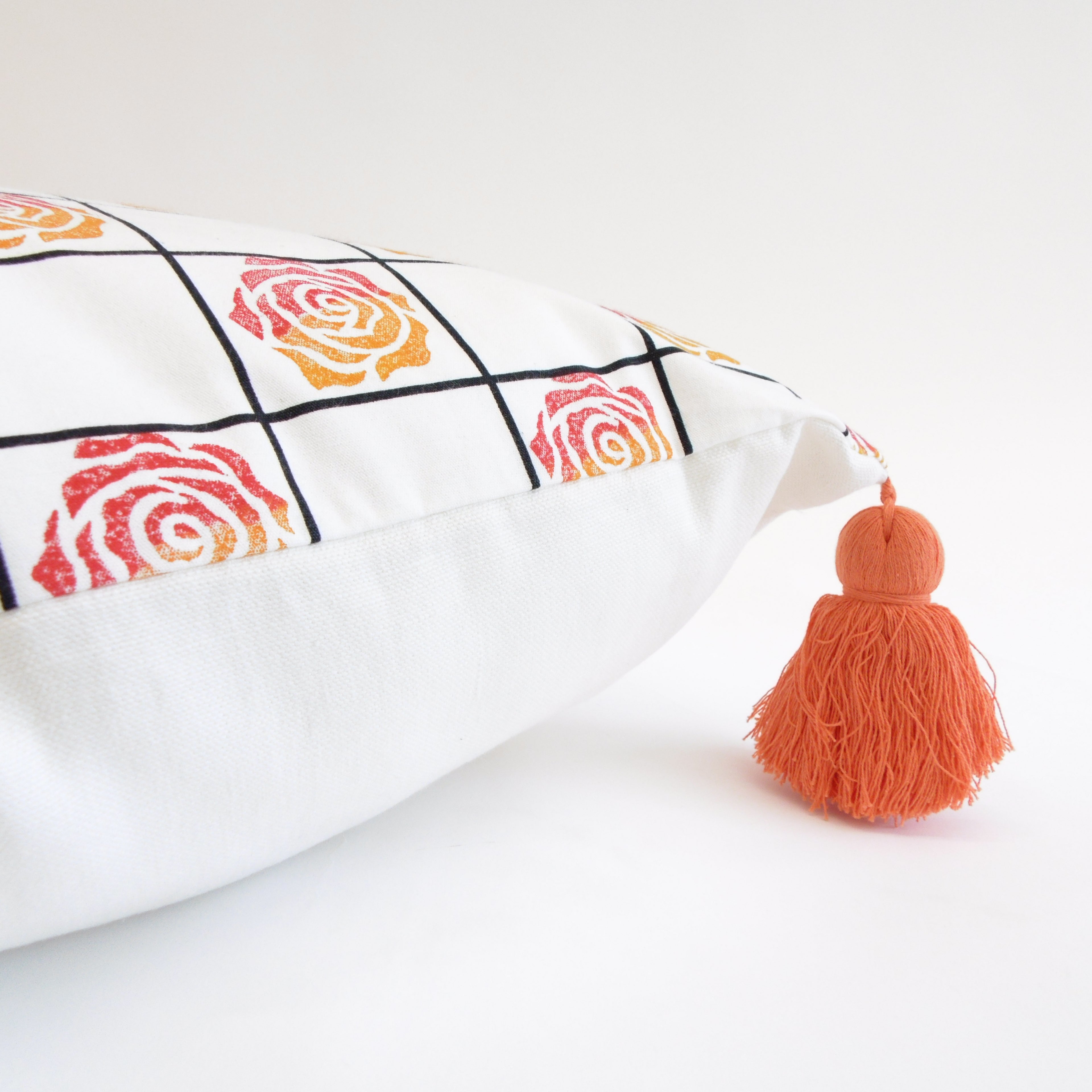 Decorative pillow with rose pattern and orange tassel on a white background