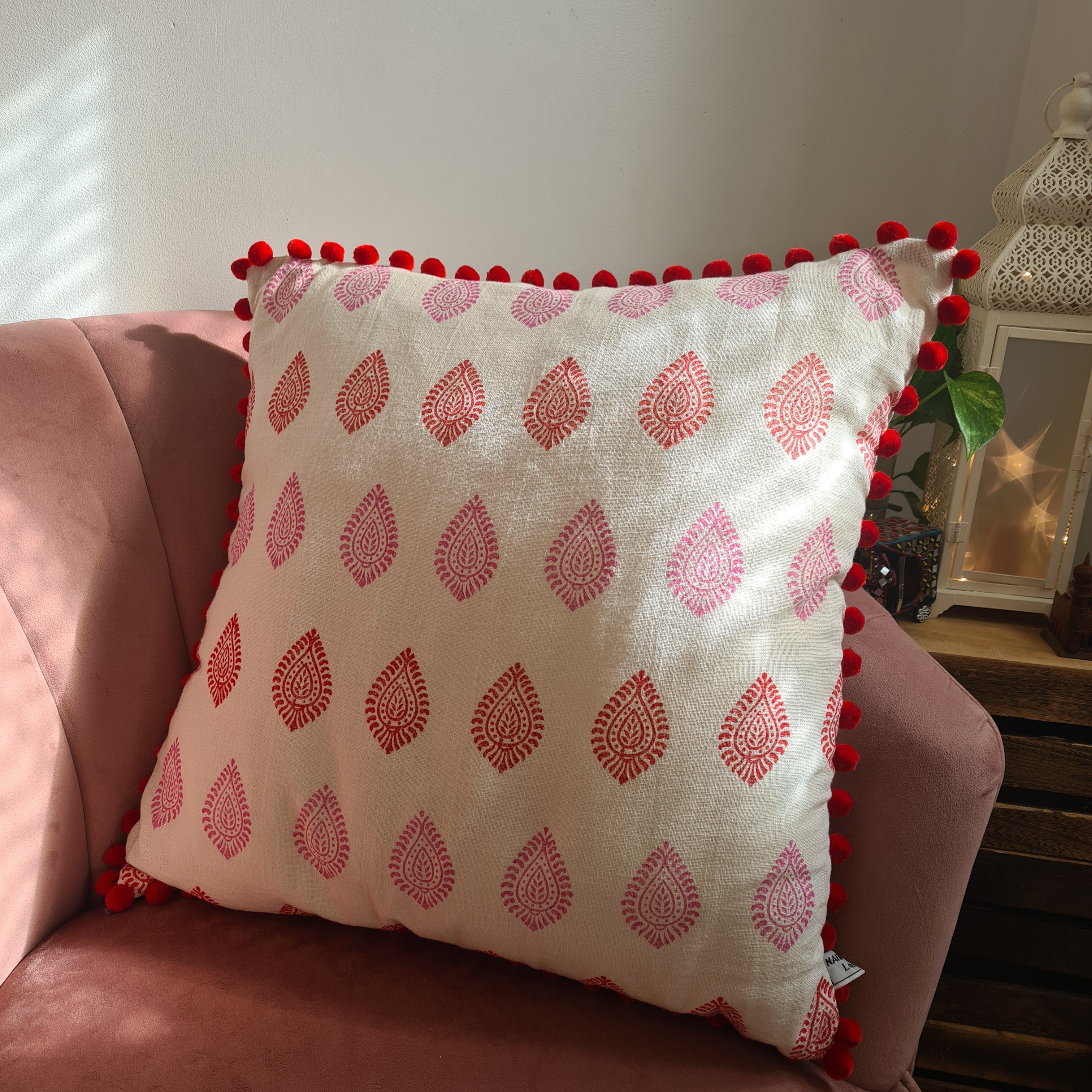 Decorative pillow with red pattern and pom-pom trim on a pink couch.
