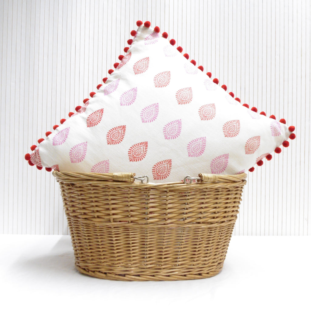 Wicker basket with a decorative pillow featuring red patterns on a white background