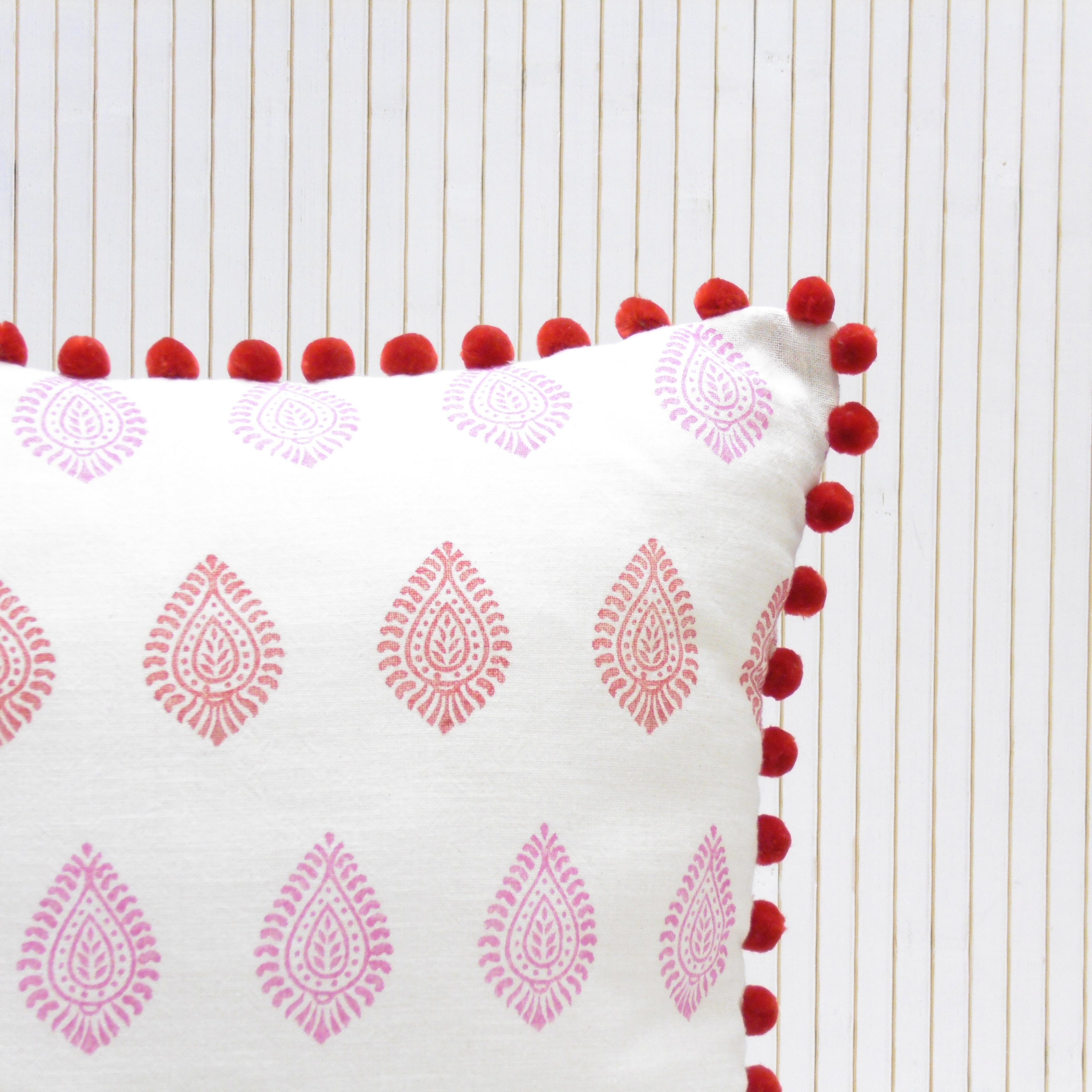 Decorative pillow with pink patterns and red pom-poms on a white background