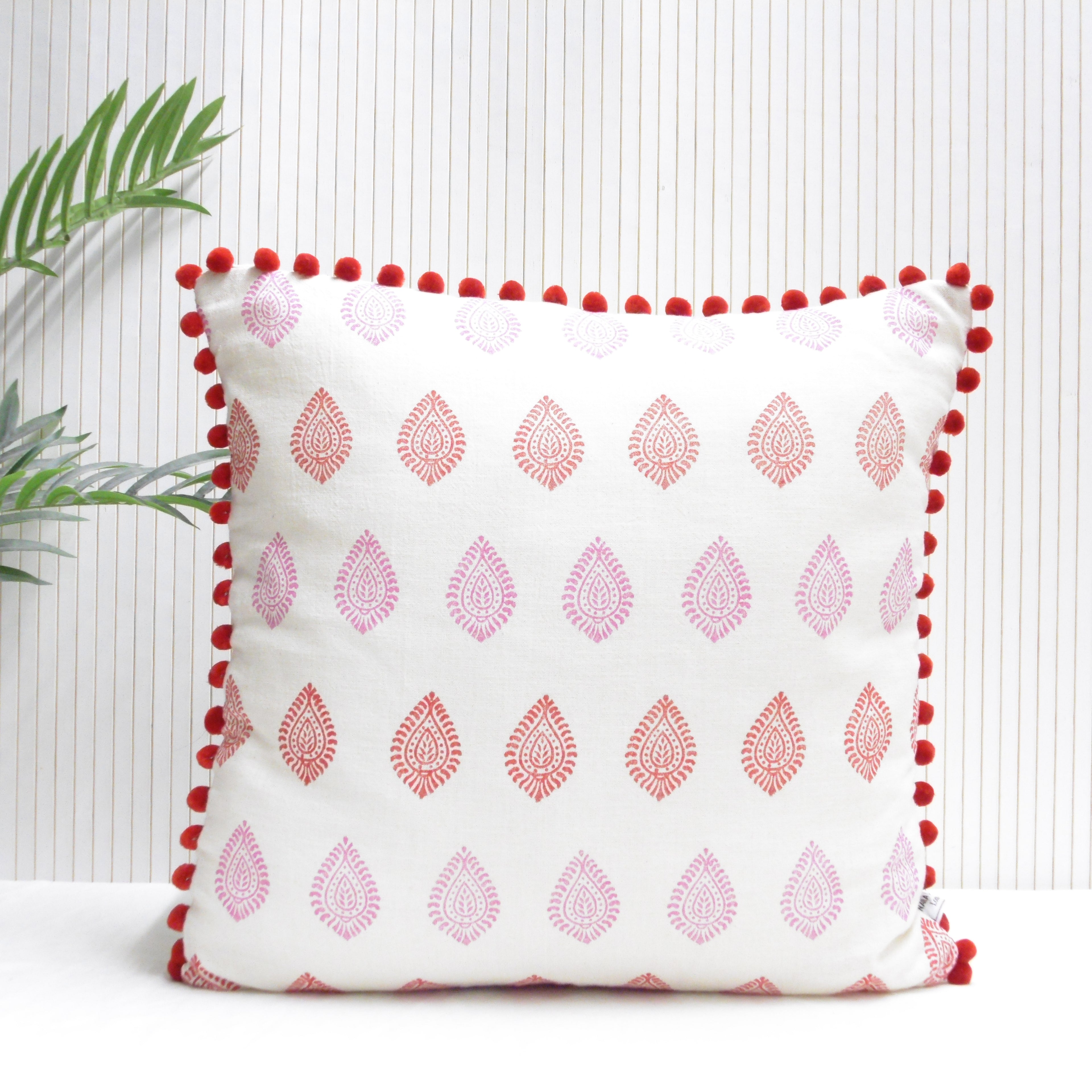 Decorative pillow with red patterns and pom-pom trim on a white background